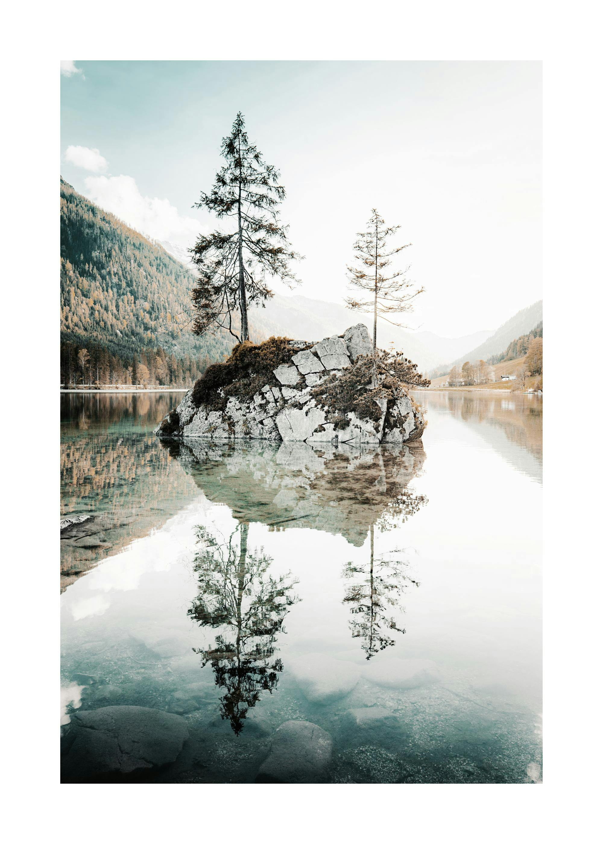 Póster de un islote rocoso con dos pinos en un lago de aguas cristalinas que reflejan el cielo y las montañas.