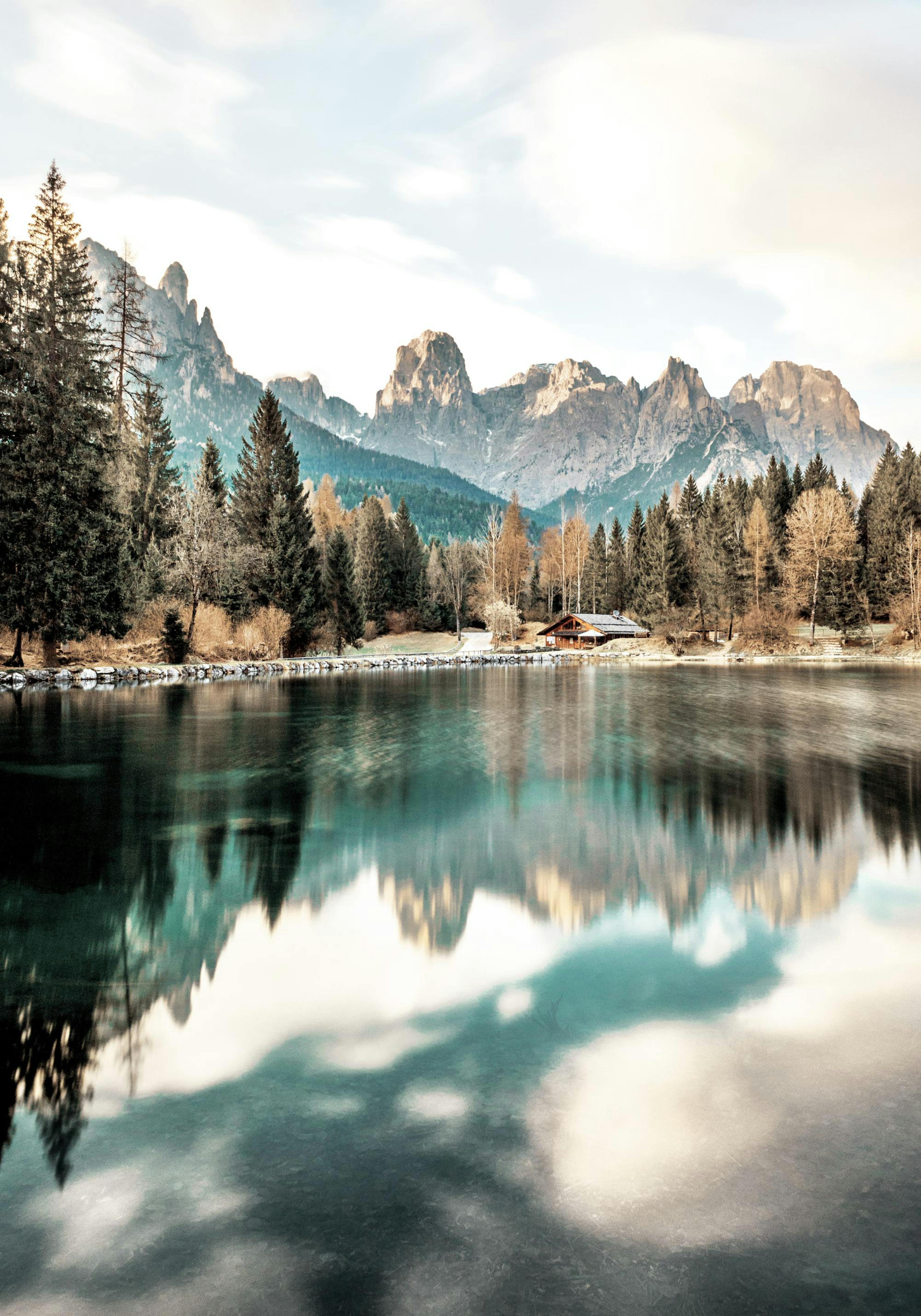 Ein Poster eines Bergsees mit Nadelbäumen, einer Hütte und schneebedeckten Gipfeln, die sich im Wasser spiegeln.