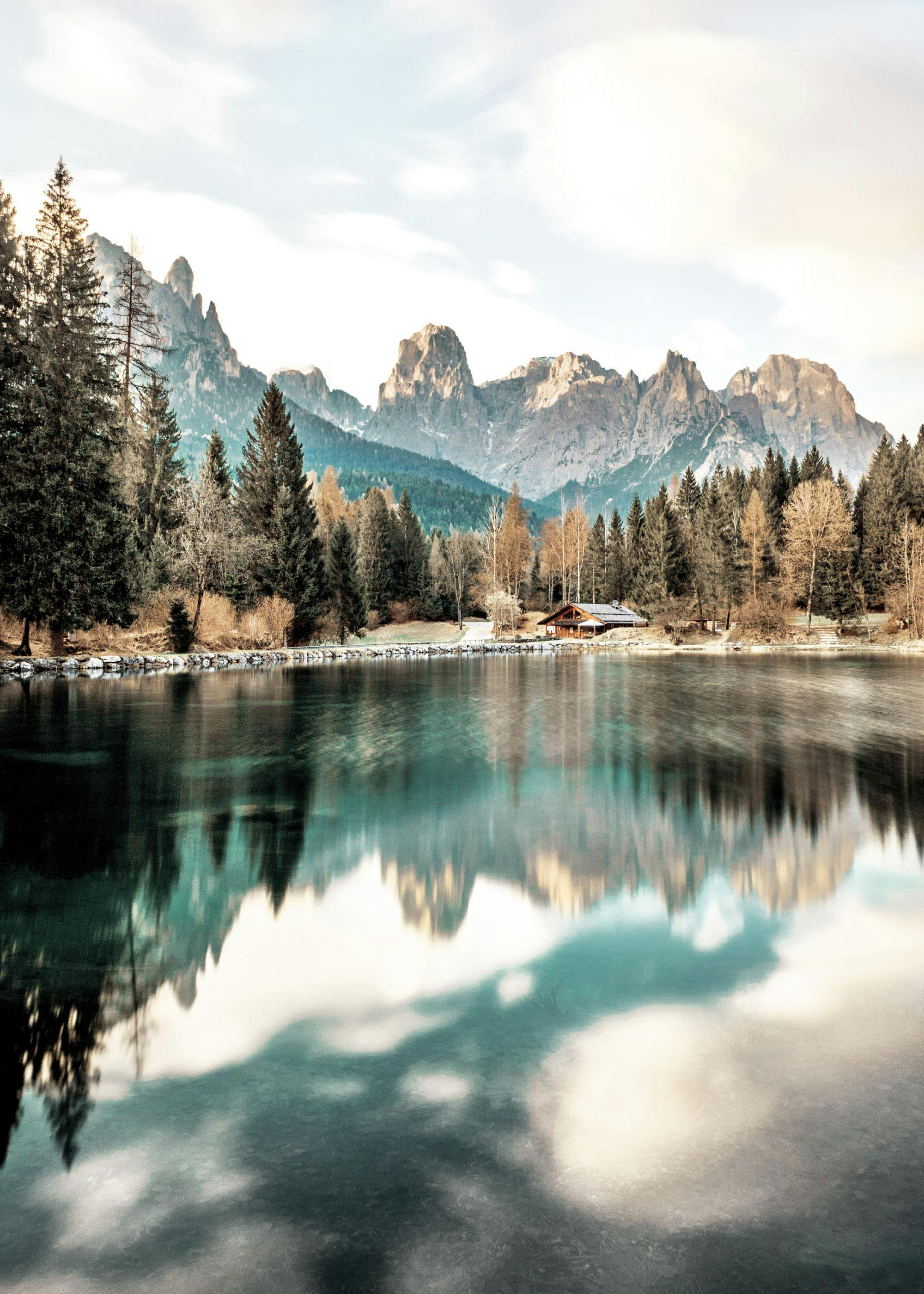 Un poster di un lago alpino con cime montuose rocciose e pini che si riflettono sullacqua blu-verde.