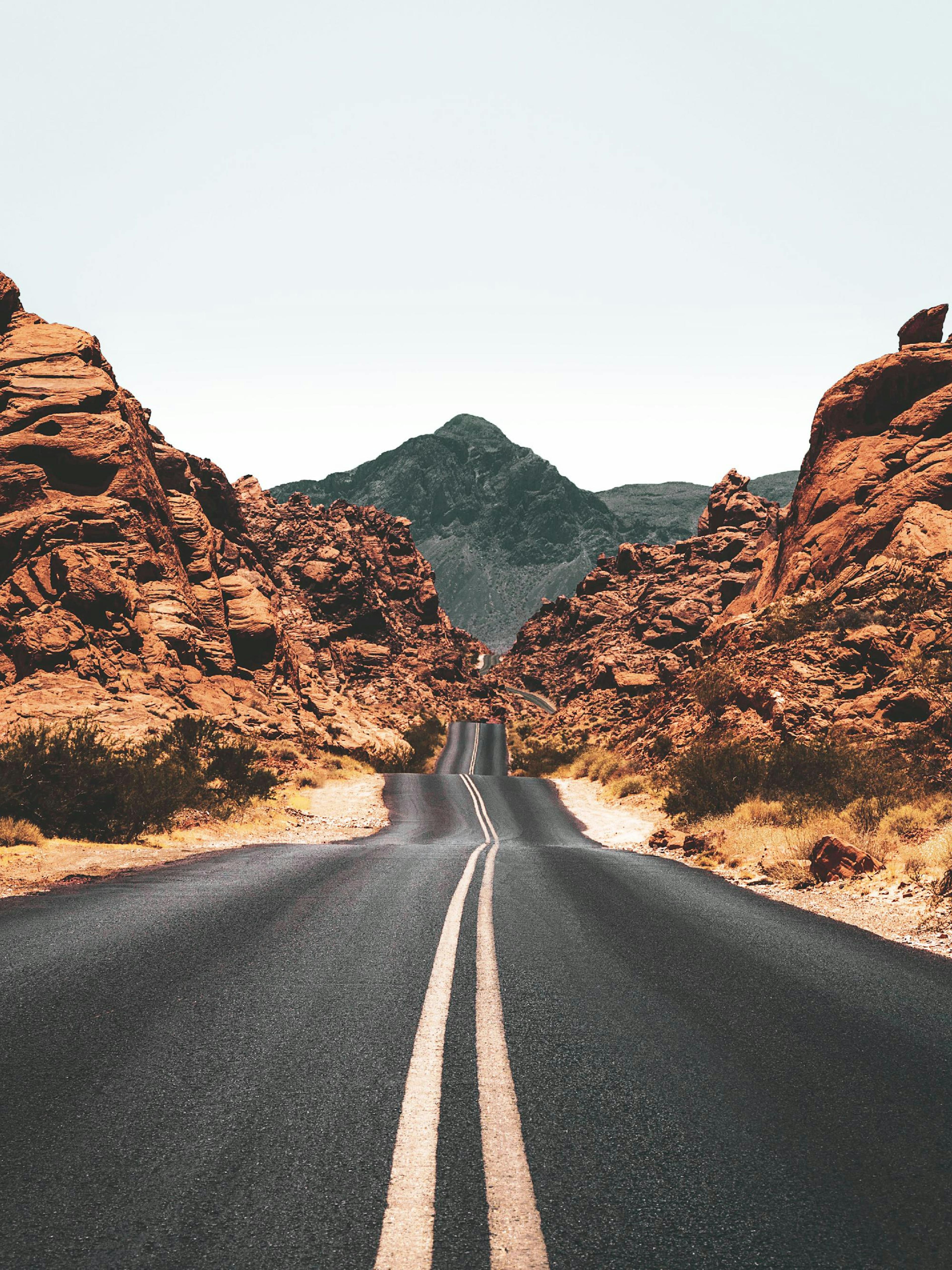 En plakat af en snoet vej gennem et ørkenlandskab med røde klipper og en mørk bjergtop i baggrunden.