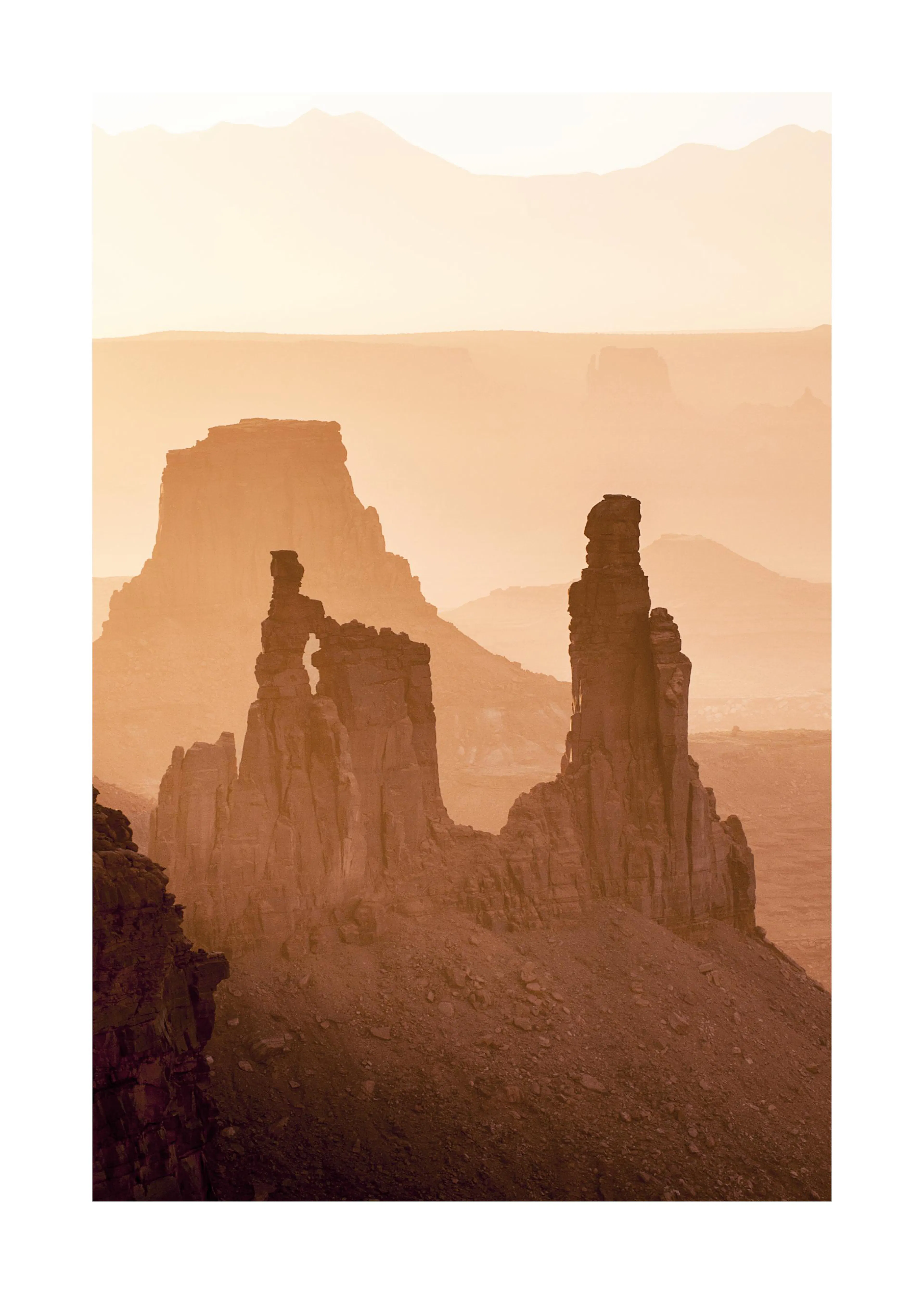 Poster: Eine Wüstenlandschaft mit großen, hohen Felssäulen und Tafelbergen in warmen Brauntönen, bei Sonnenuntergang.