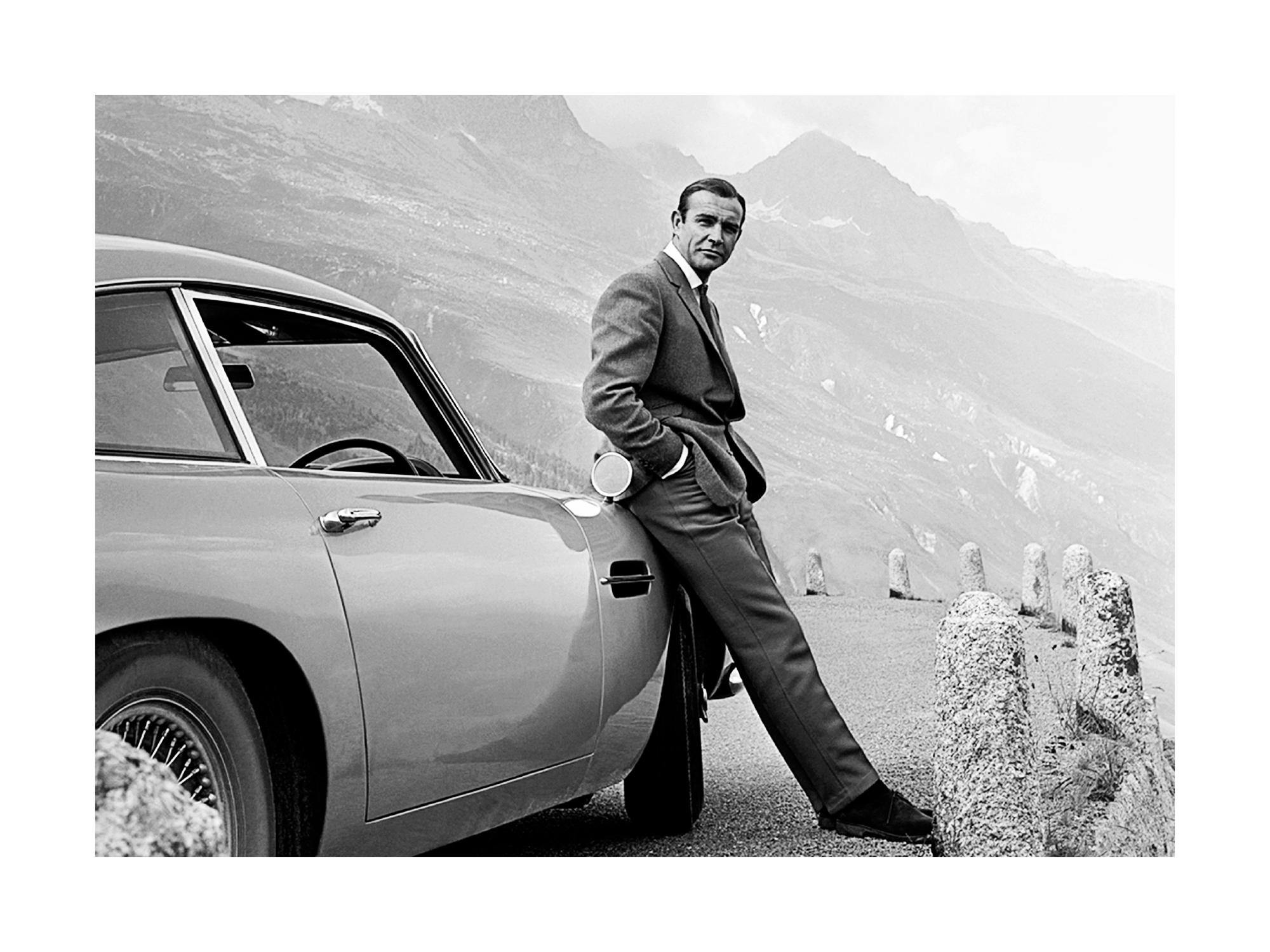 Poster: Sean Connery als James Bond, lässig an einen Aston Martin gelehnt, mit Berglandschaft im Hintergrund.