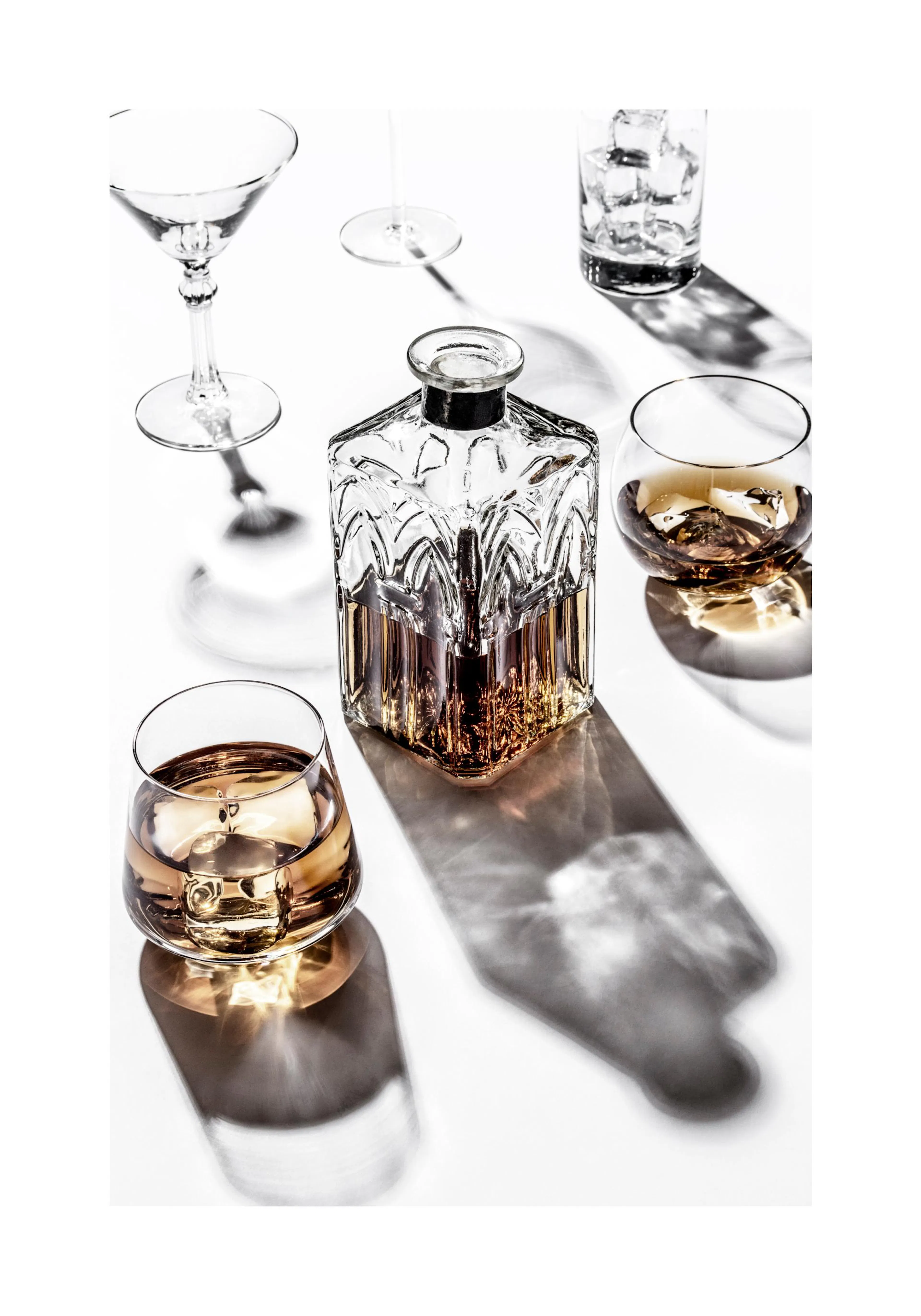 A poster featuring a crystal decanter and two whisky glasses with amber liquid, casting long shadows on a white surface.