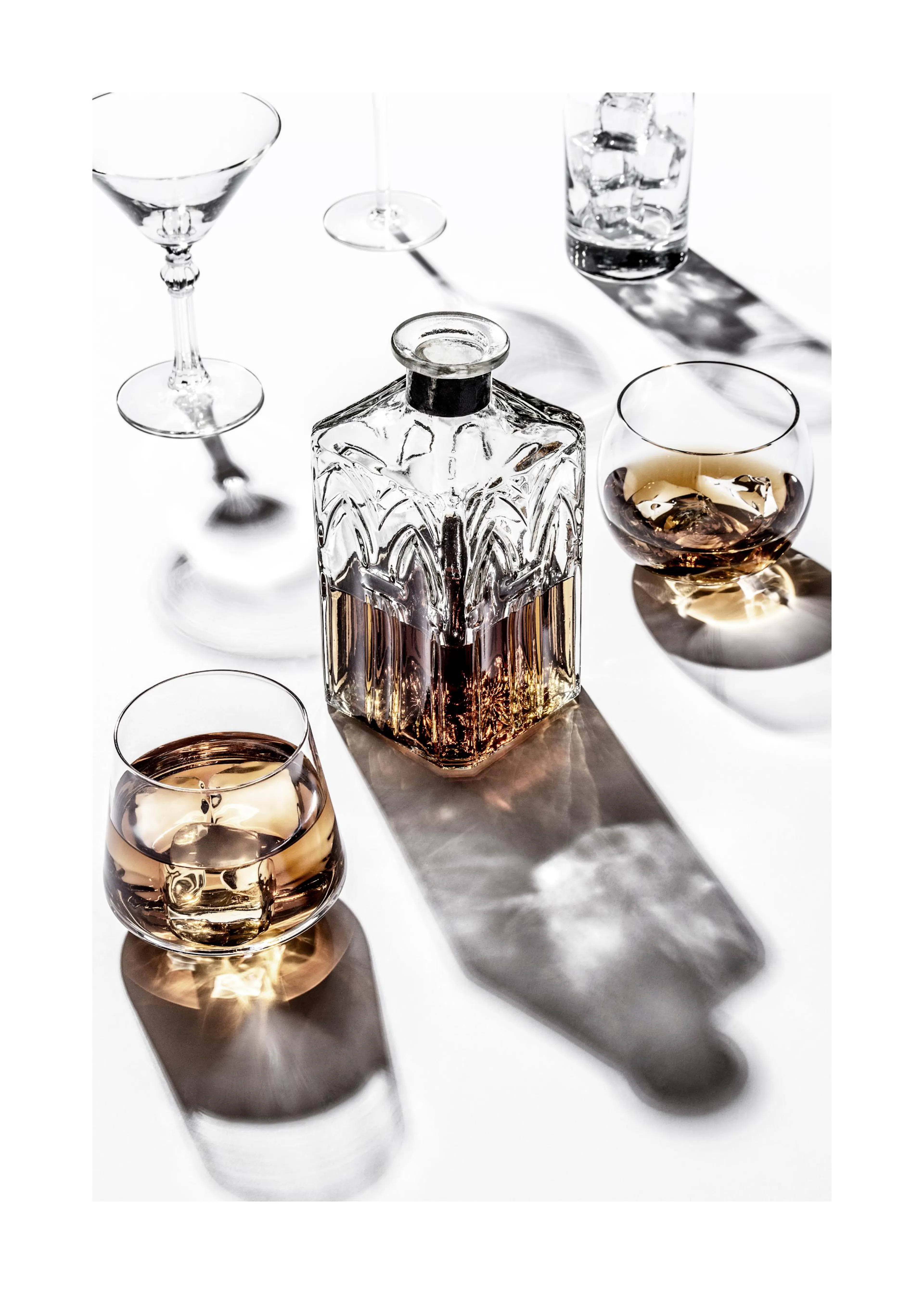 Un poster di una bottiglia di liquore in vetro intagliato con due bicchieri di whisky e bicchieri vuoti su sfondo bianco.