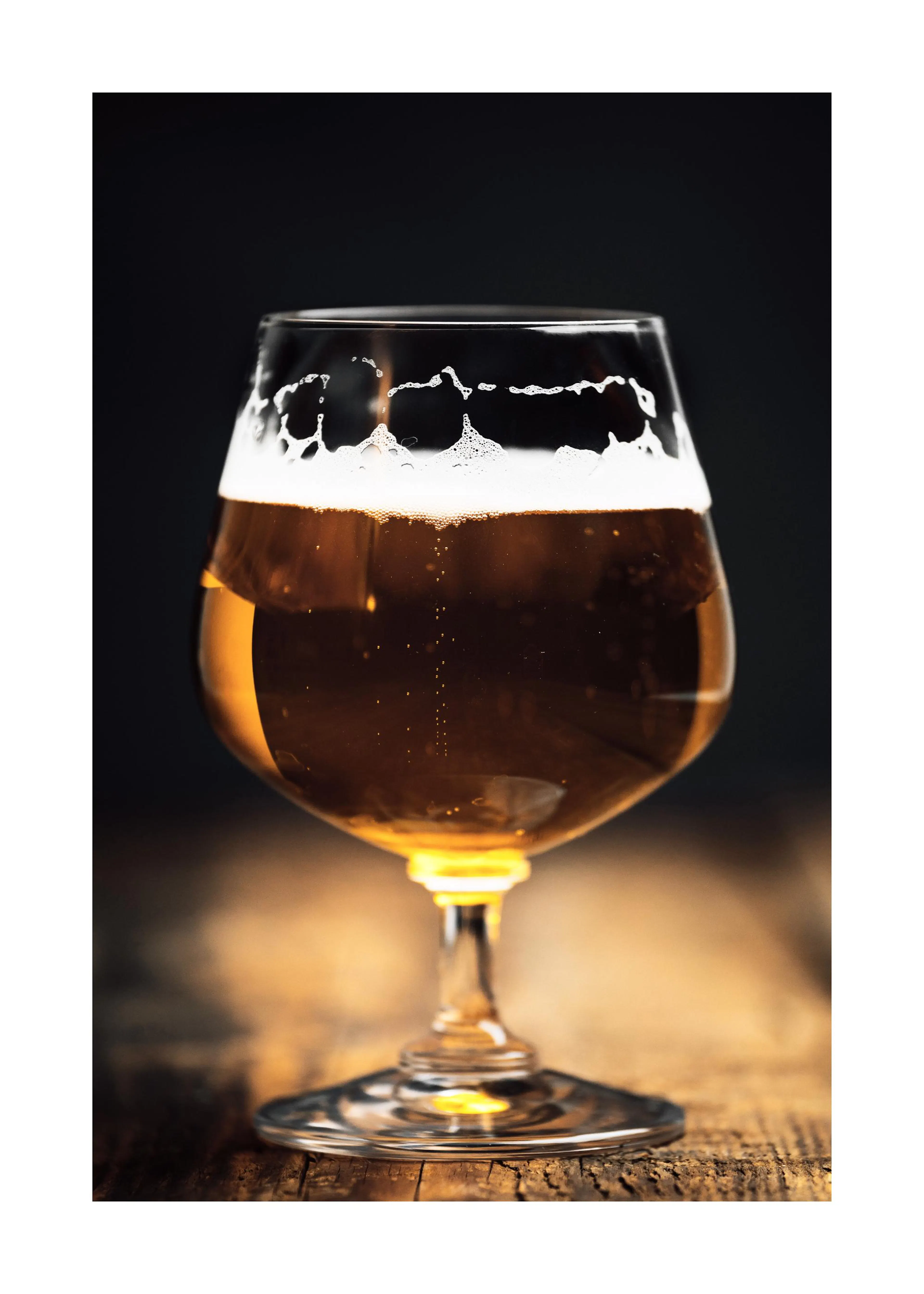 Een poster van een glas bier met schuimkraag op een houten tafel, met een donkere achtergrond.