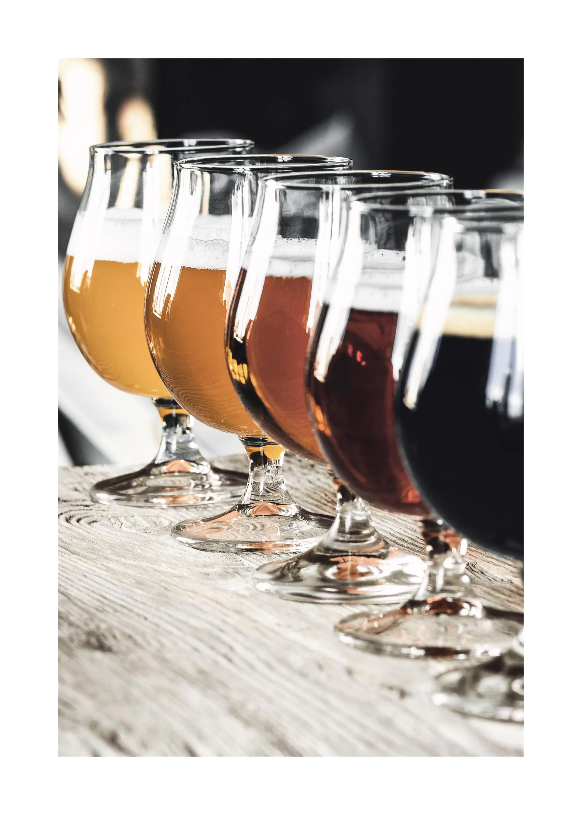 A poster featuring five glasses of beer from light amber to dark brown, lined up on a rustic wooden surface.