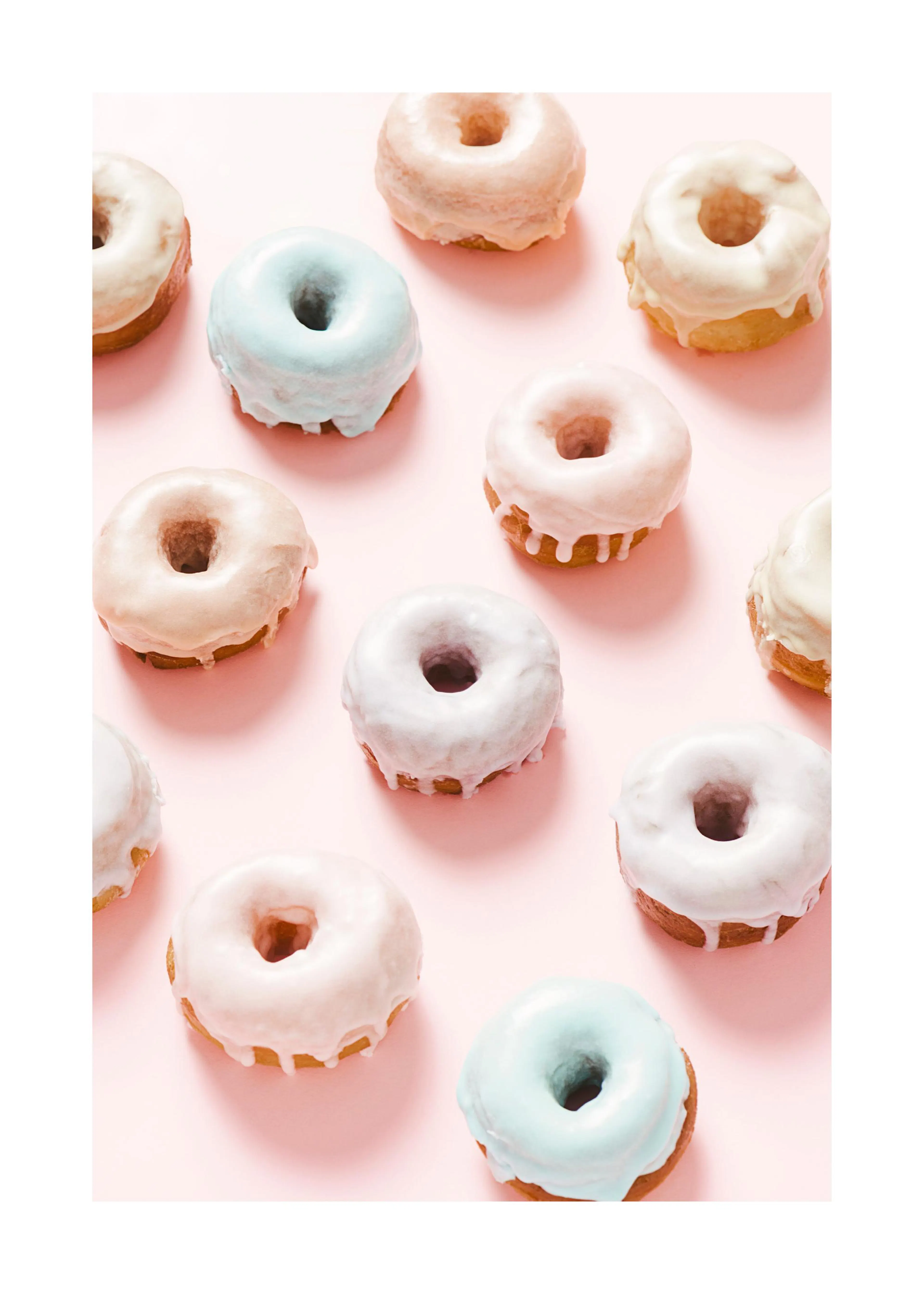Un poster représentant des donuts colorés, glacés de rose, blanc et bleu pâle, sur un fond rose uni.