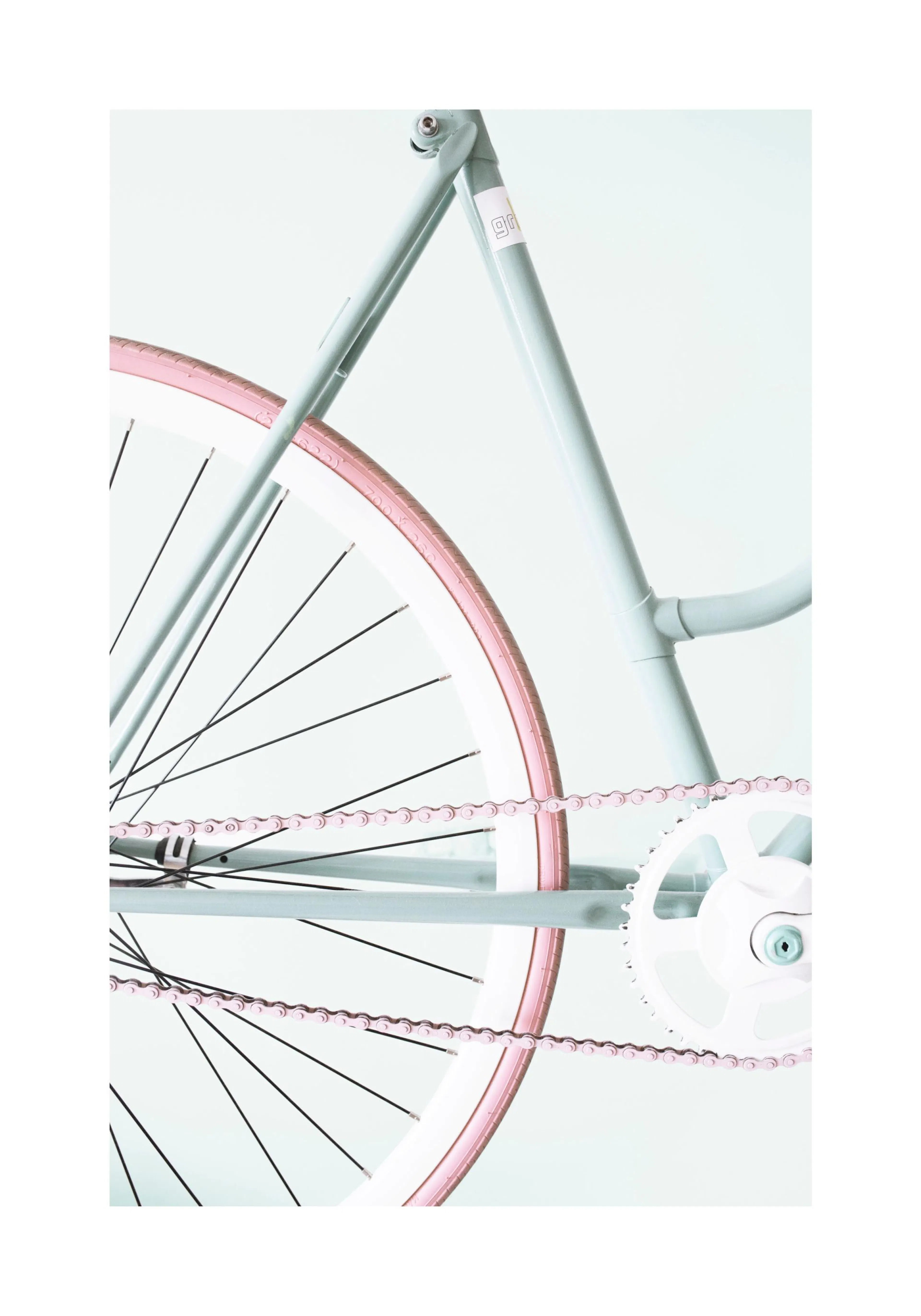 A poster featuring a close-up of a mint green bicycle with a pink tire and chain, on a light background.