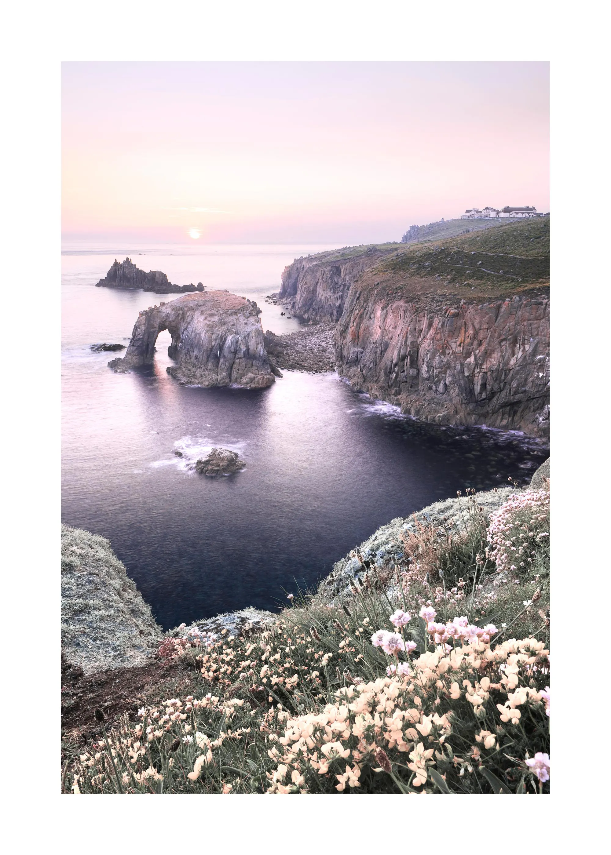 Poster einer sonnigen Küstenlandschaft mit rosafarbenen Blumen im Vordergrund, Klippen und einem Felsentor im Meer bei Sonnenunt