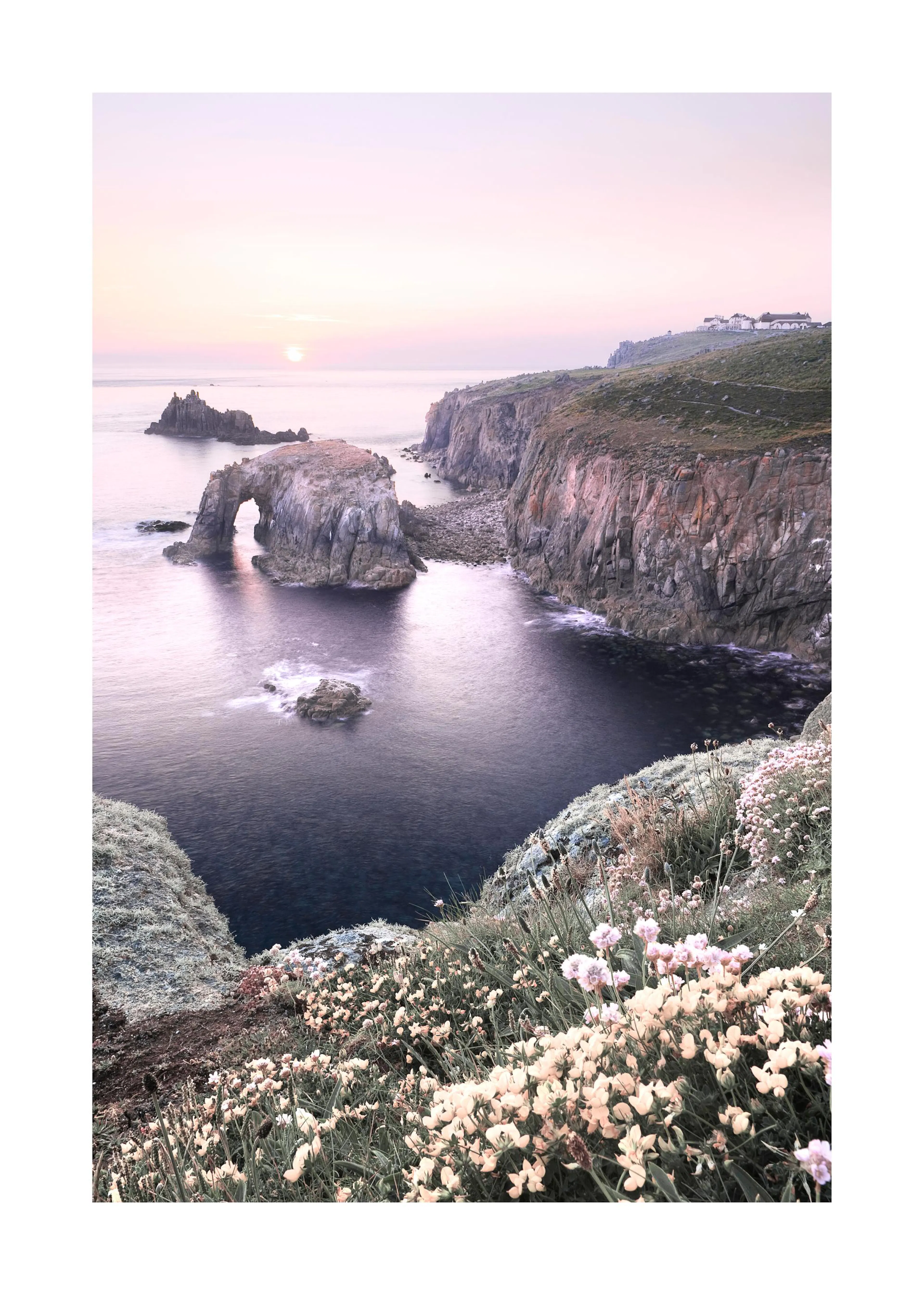 Napfelkeltét ábrázoló poster tengeri tájjal, sziklákkal, sziklaívekkel és virágokkal az előtérben.