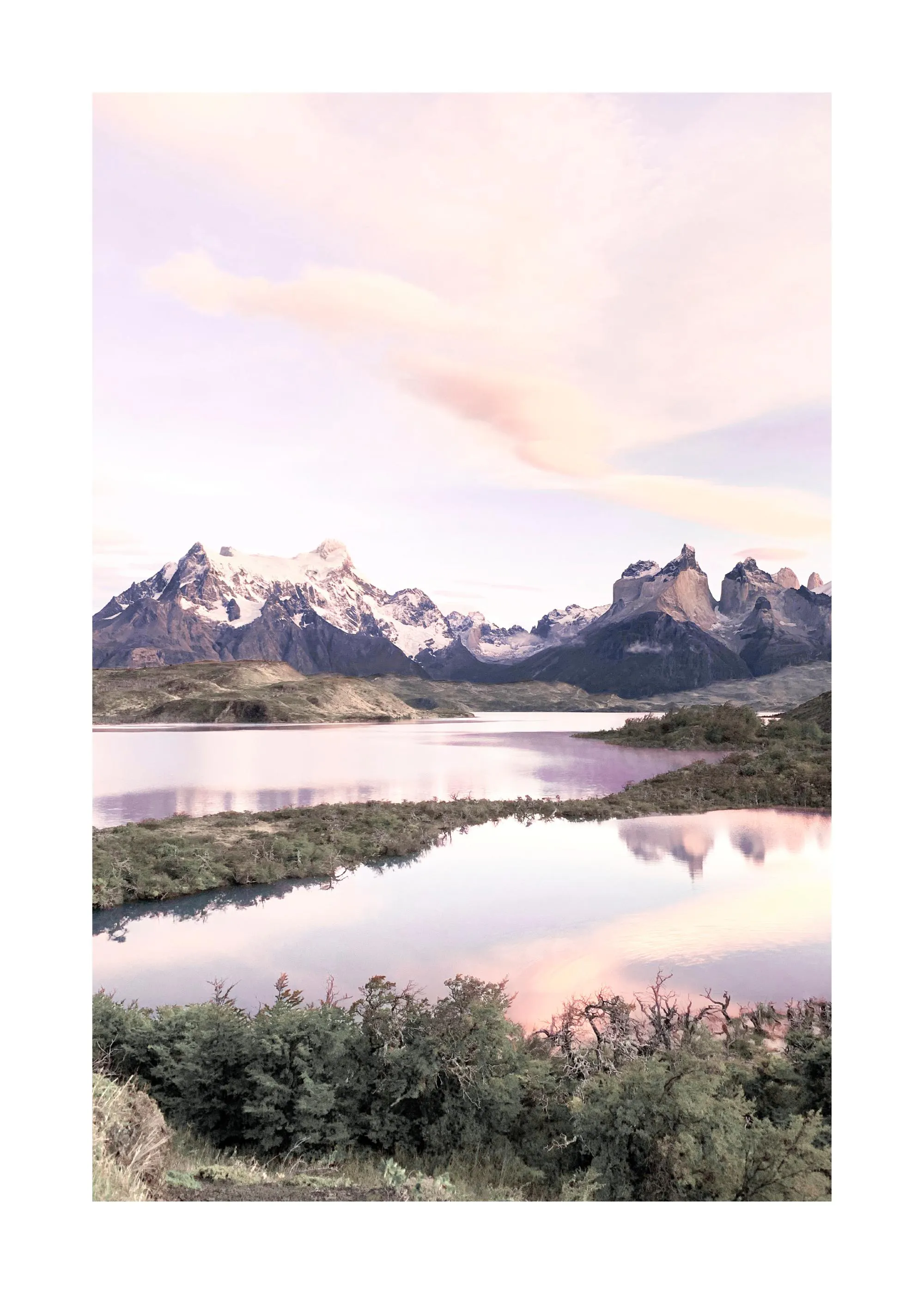 Poster: Ein ruhiger See spiegelt schneebedeckte Berge und einen rosa-lila Himmel wider, umgeben von grünen Büschen.