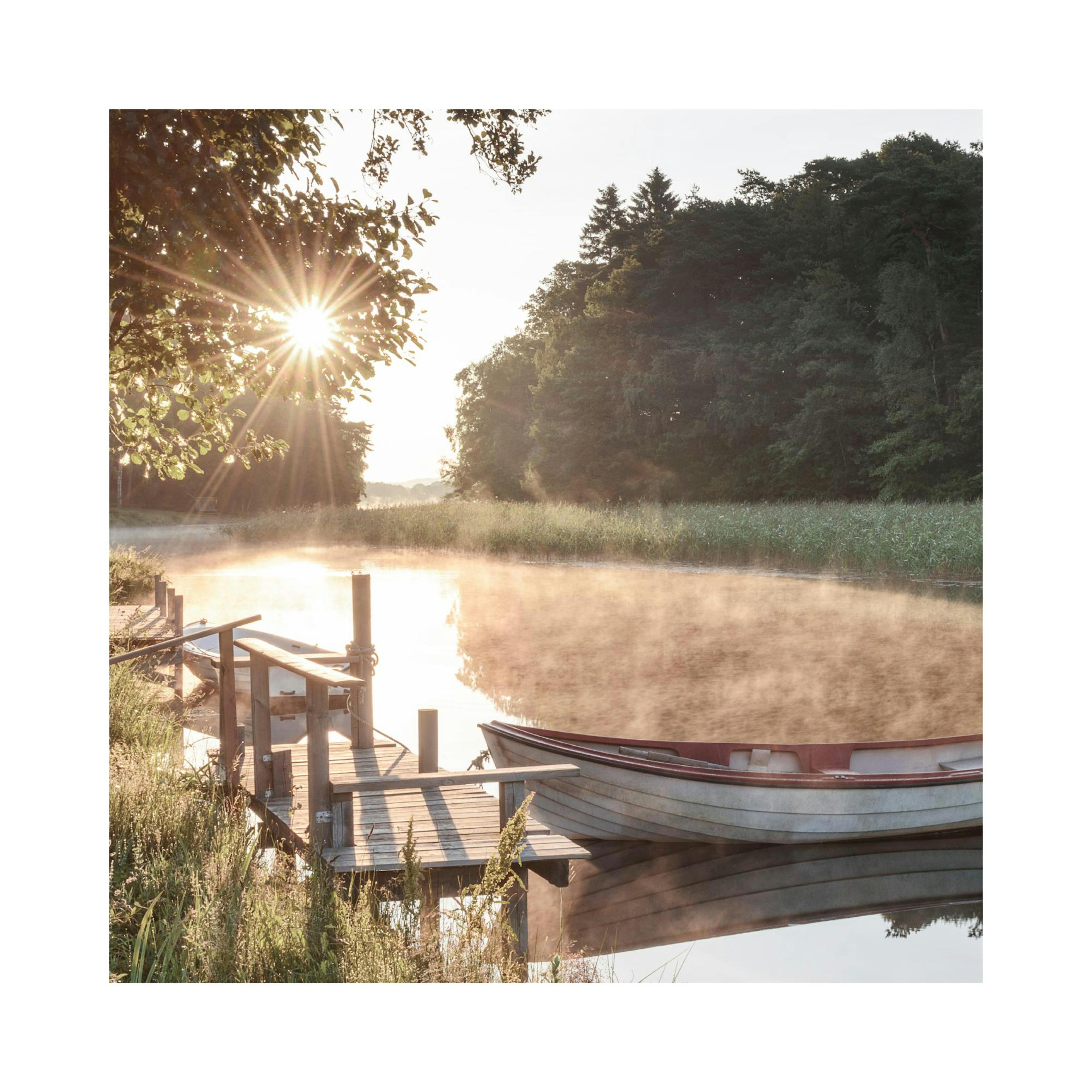 Napfelkelte a tavon, csónakkal és stéggel. A víz felett párás köd úszik, a nap sugarai áthatolnak a fákon ezen a poszteren.