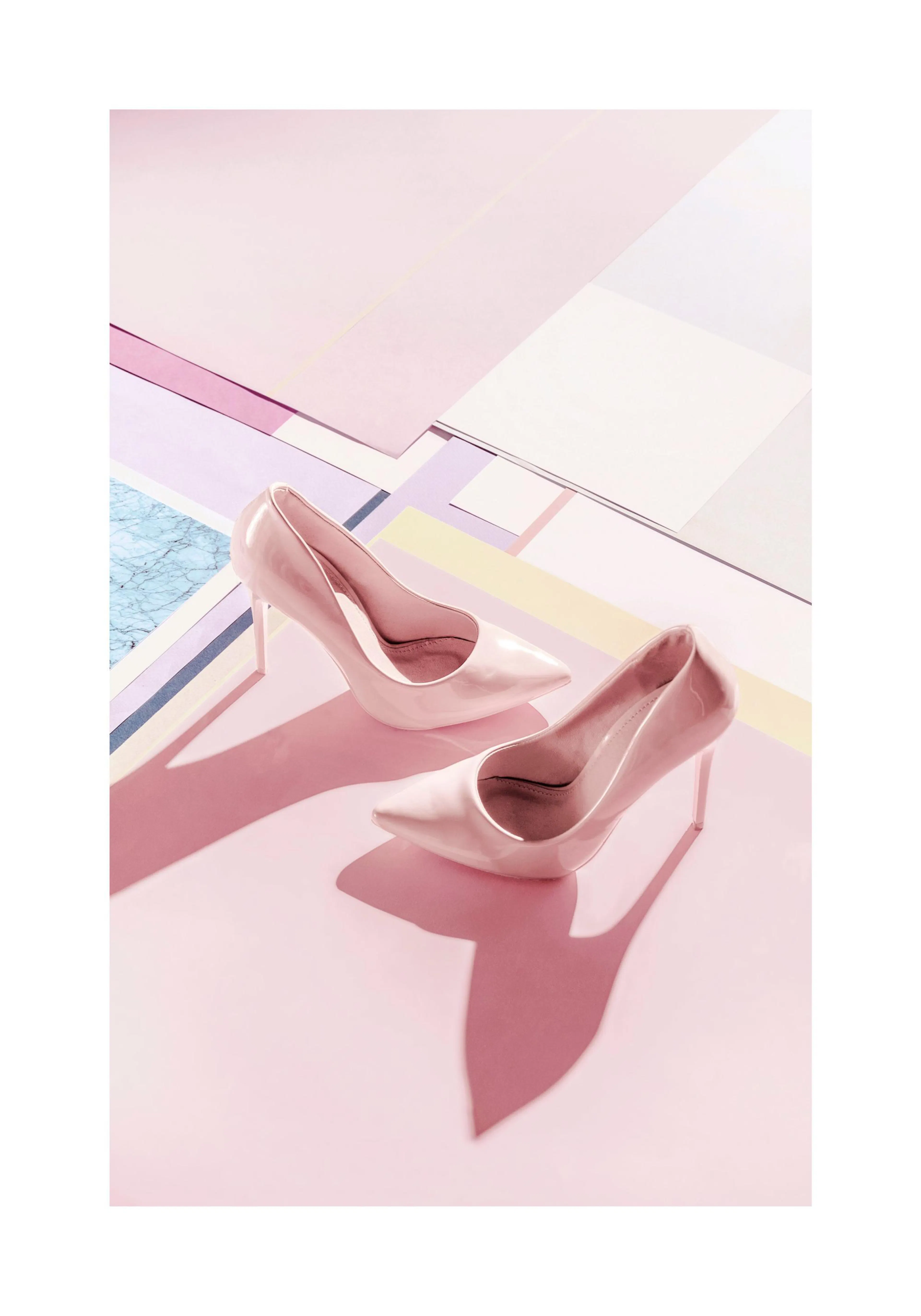 A poster featuring two light pink high heels on a pink surface with shadows, against a background of pastel geometric shapes and