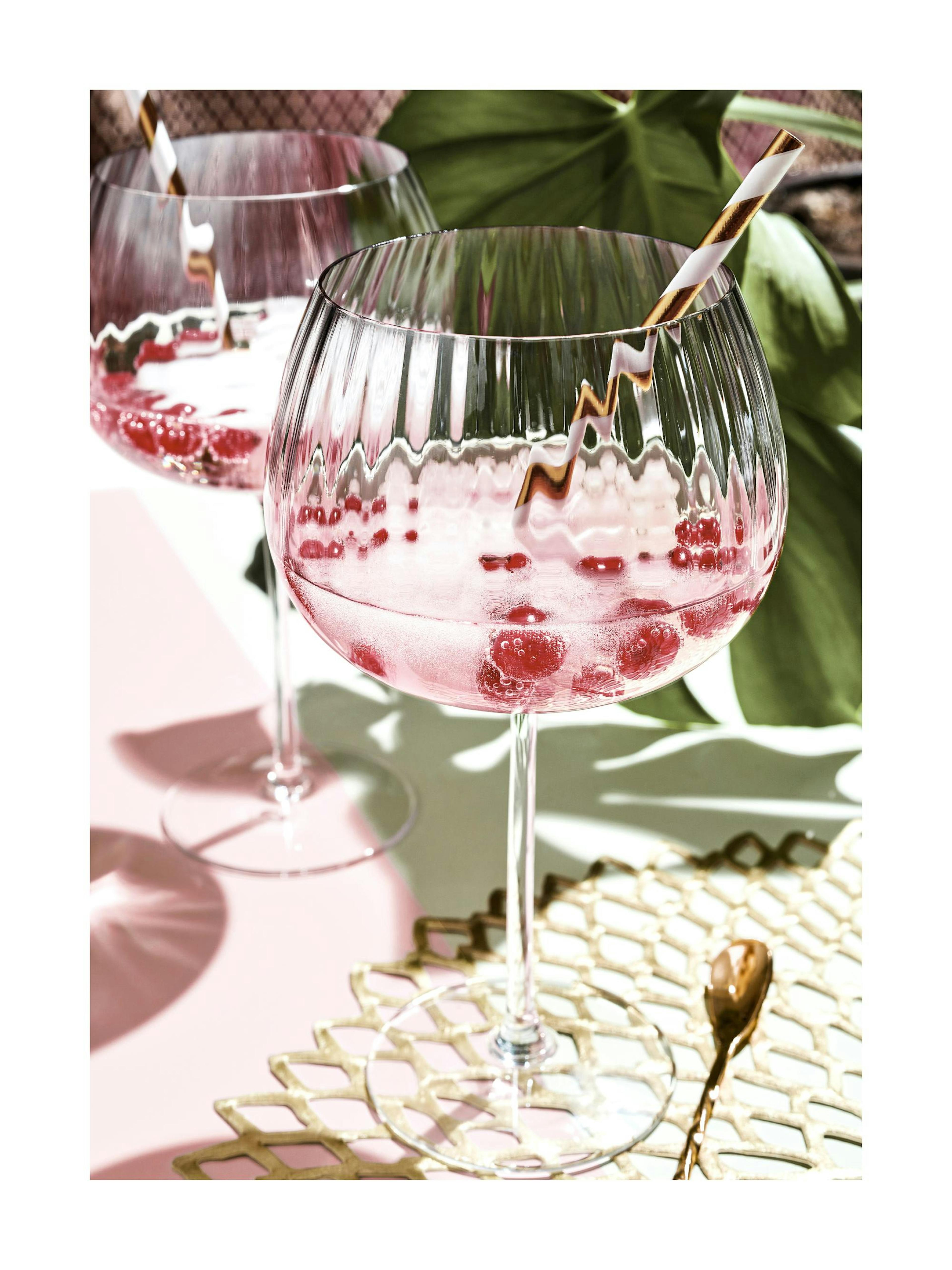 A poster featuring a close-up of two pink cocktails with raspberries and striped straws, on a light pink table.