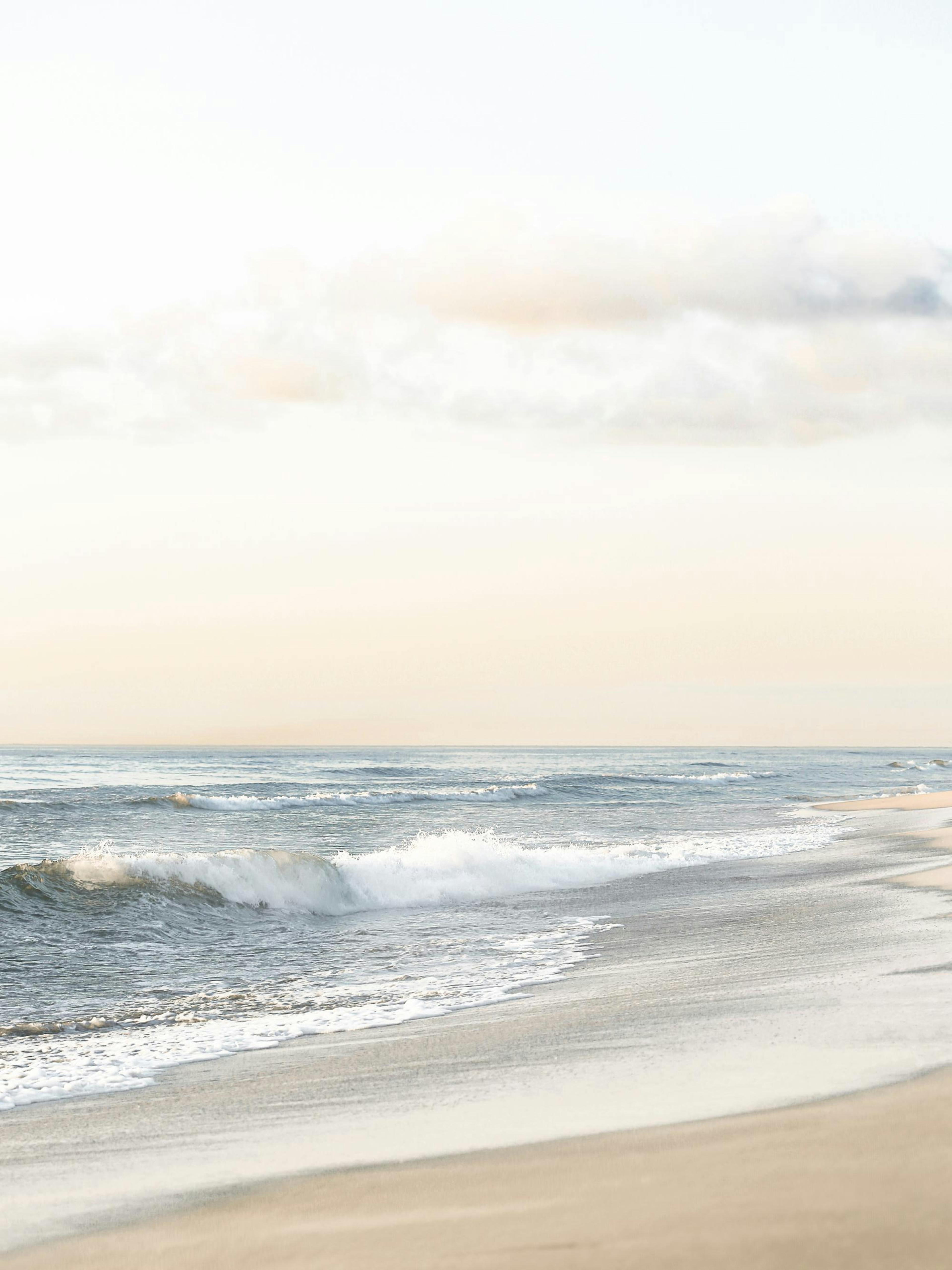 Póster de una serena playa con arena clara y olas suaves rompiendo en la orilla bajo un cielo pálido.