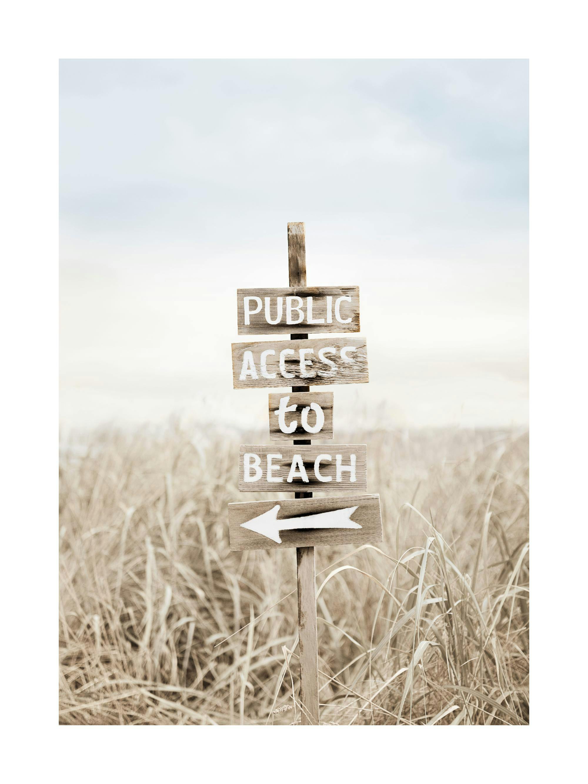Een poster van een houten bord met de tekst Public Access to Beach en een pijl, in een veld van droog gras.