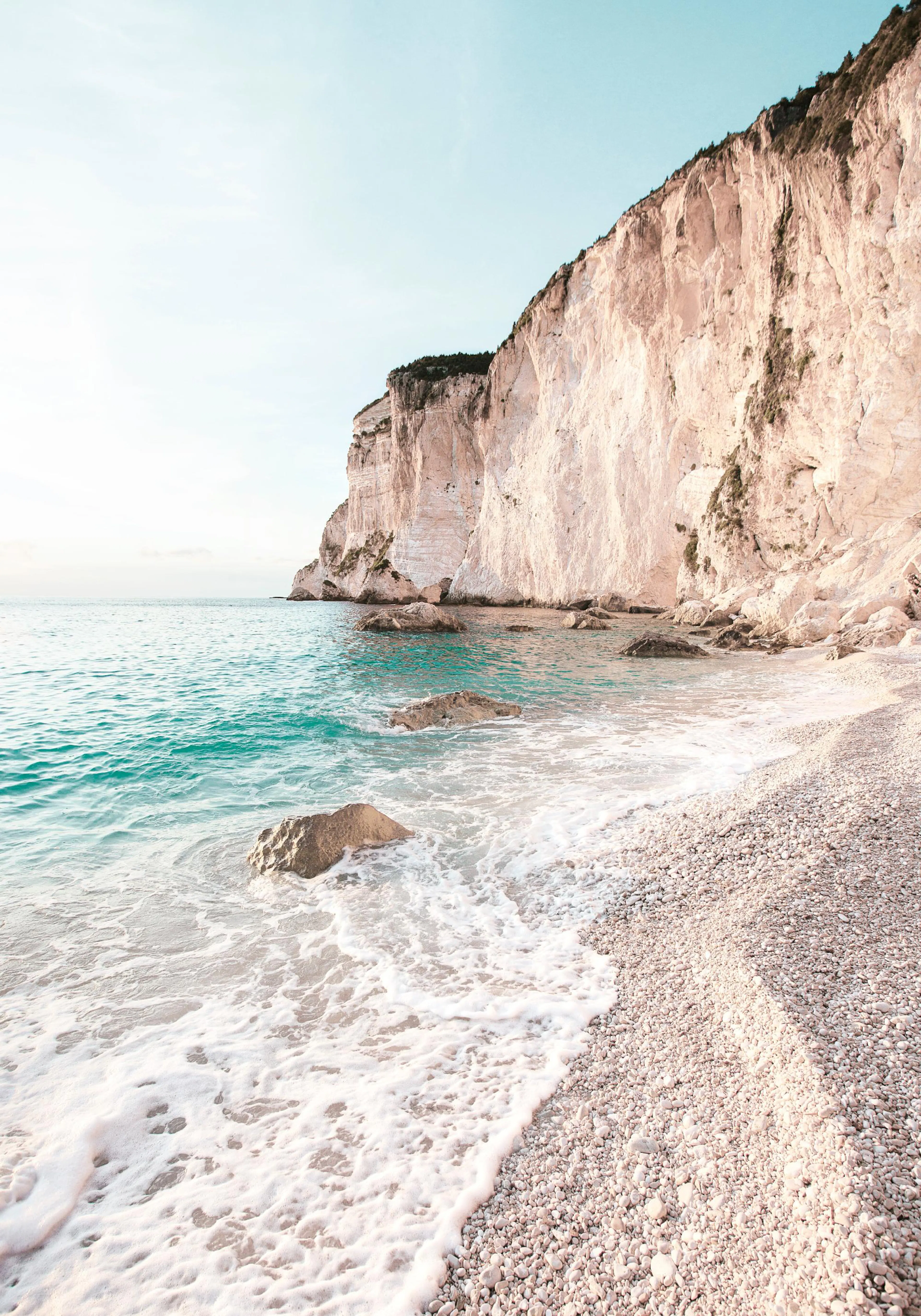 A poster featuring a white cliff face overlooking a turquoise sea with white foamy waves on a pebble beach.