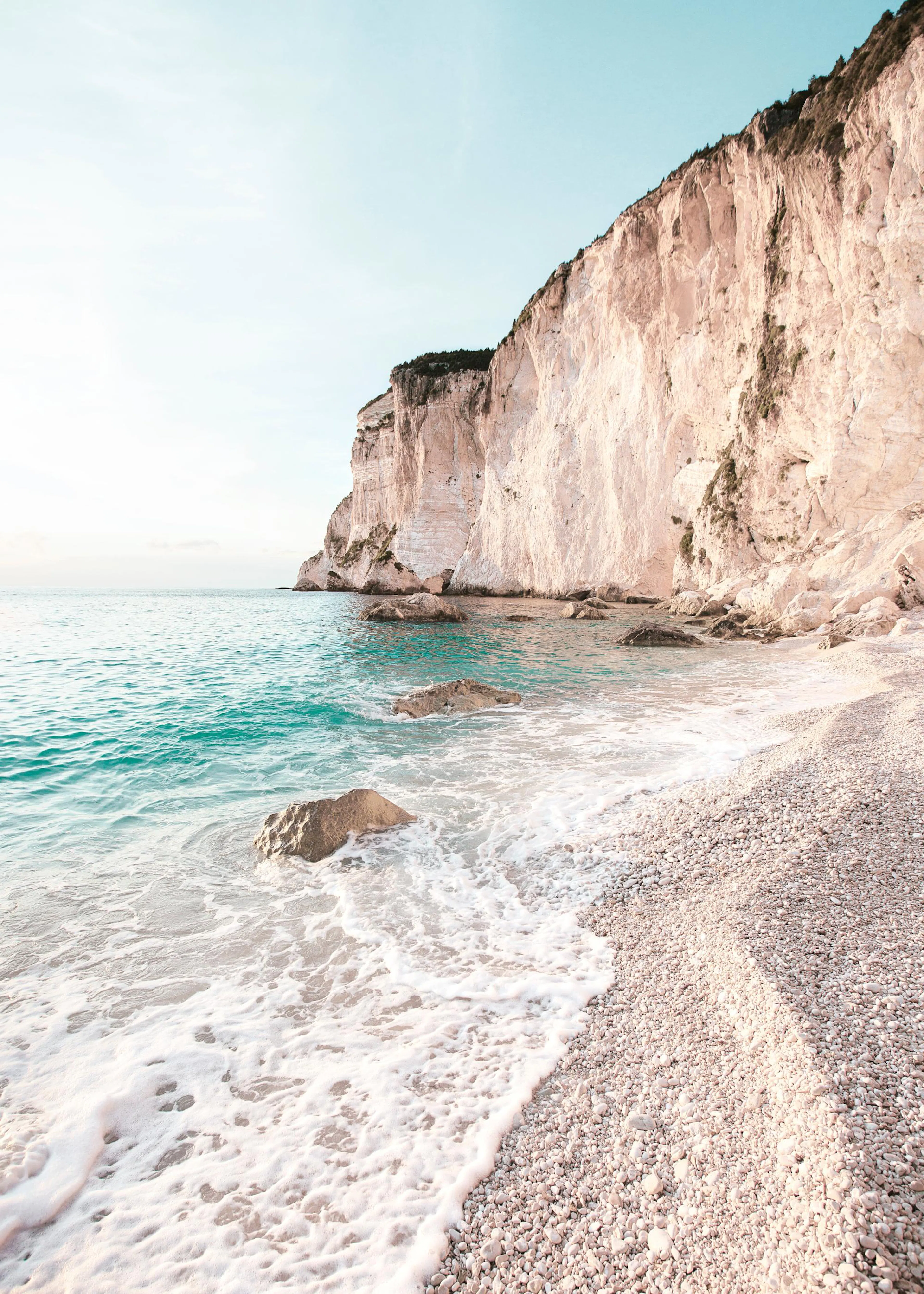 Poster einer felsigen Küste mit türkisfarbenem Meer und weißem Schaum, der auf einen Kieselstrand trifft.