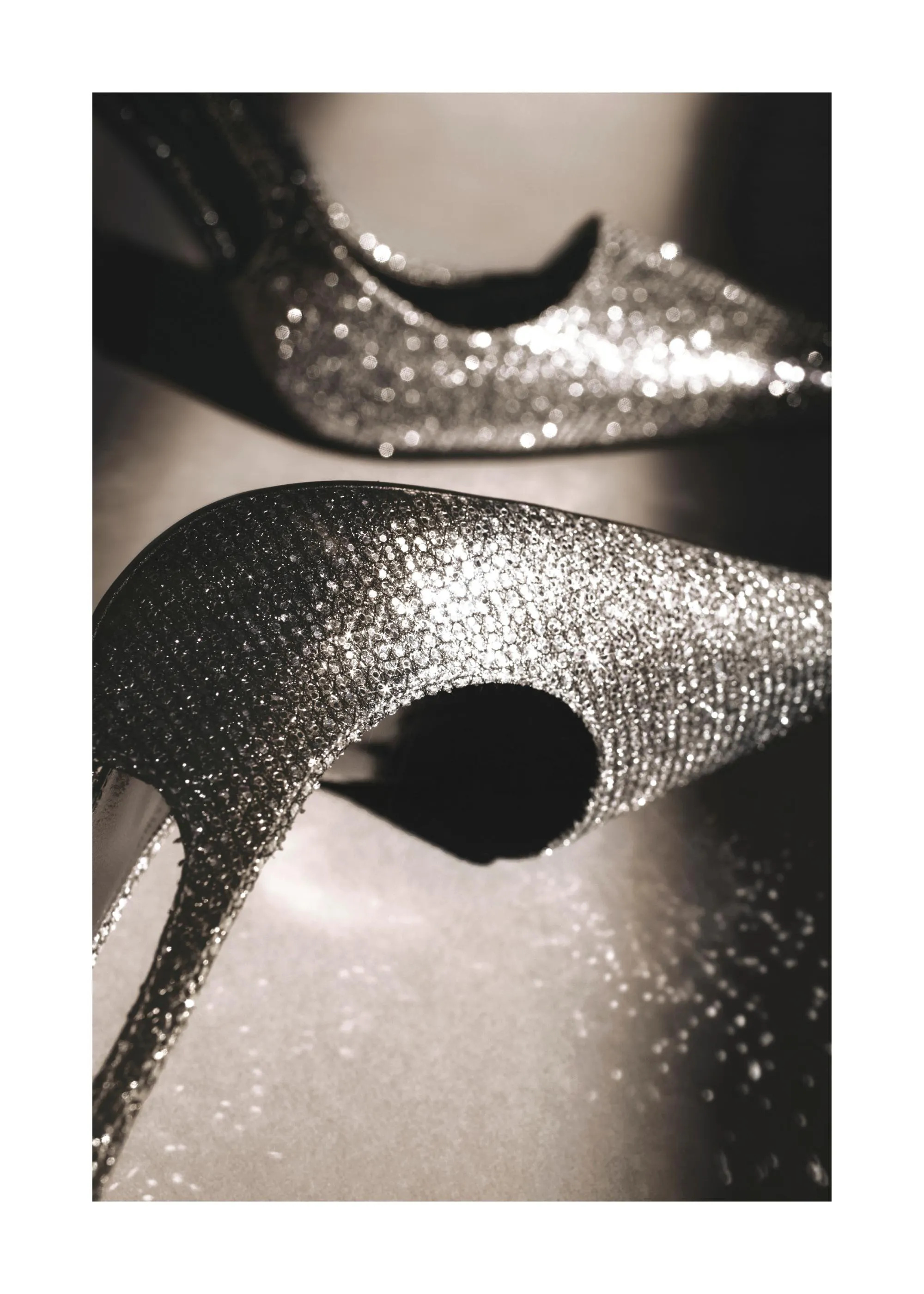 Juliste kahdesta kimaltelevasta korkokengästä, jotka heijastavat valoa hopeanhohtoisesti tummalla taustalla.