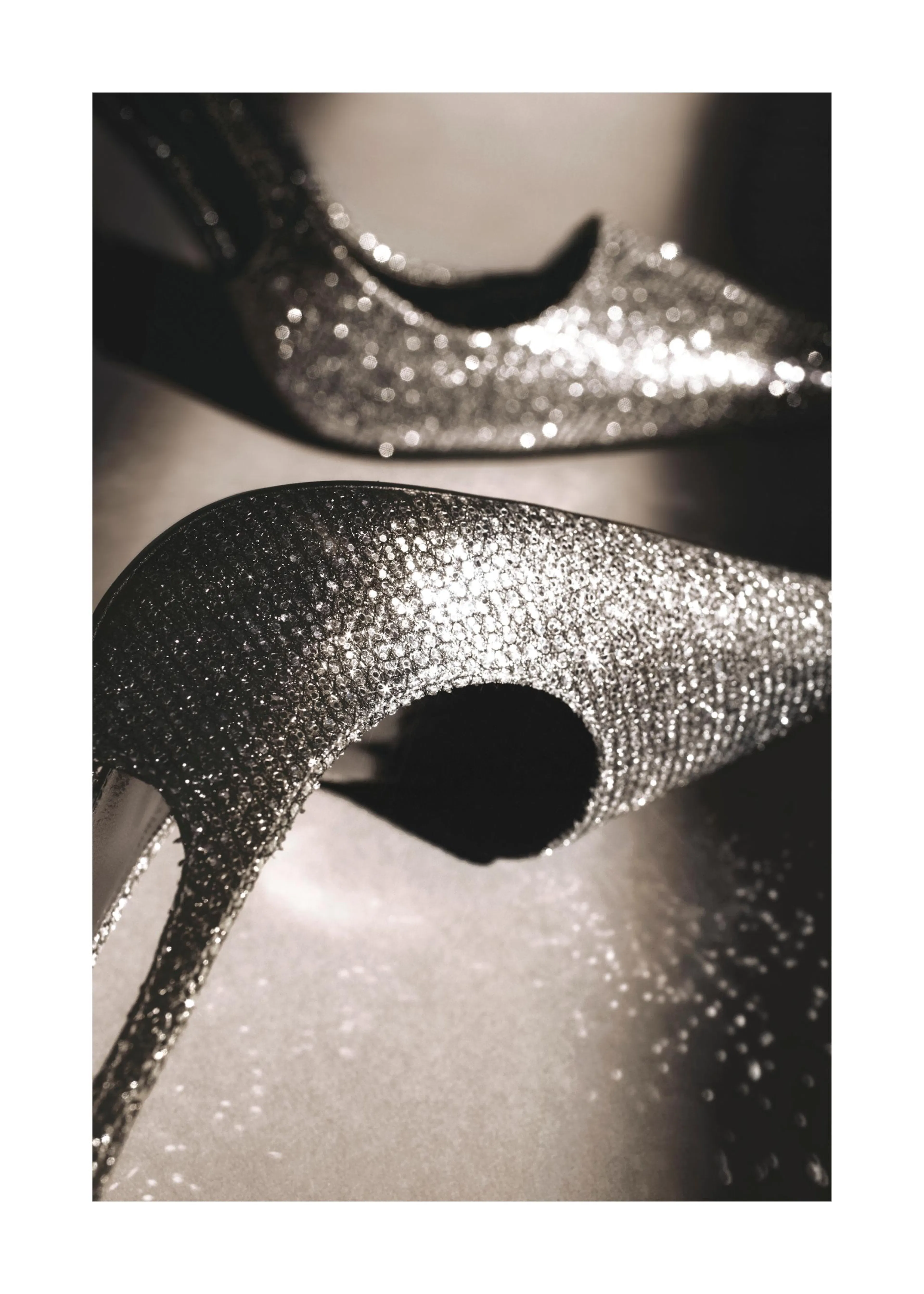 Juliste kahdesta kimaltelevasta korkokengästä, jotka heijastavat valoa hopeanhohtoisesti tummalla taustalla.