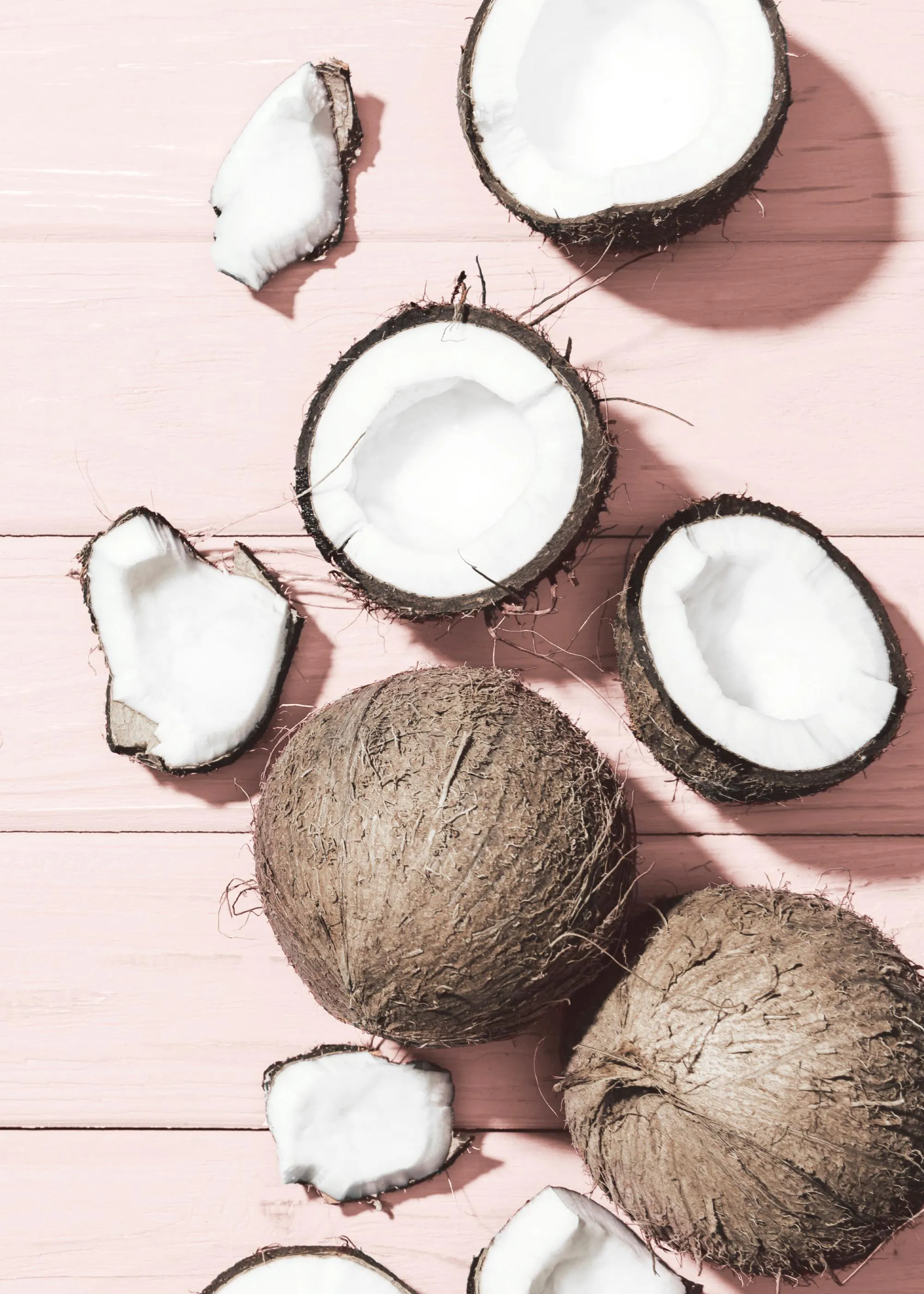 Dieses Poster zeigt ganze und aufgeschnittene Kokosnüsse auf einem rosa Holzuntergrund.