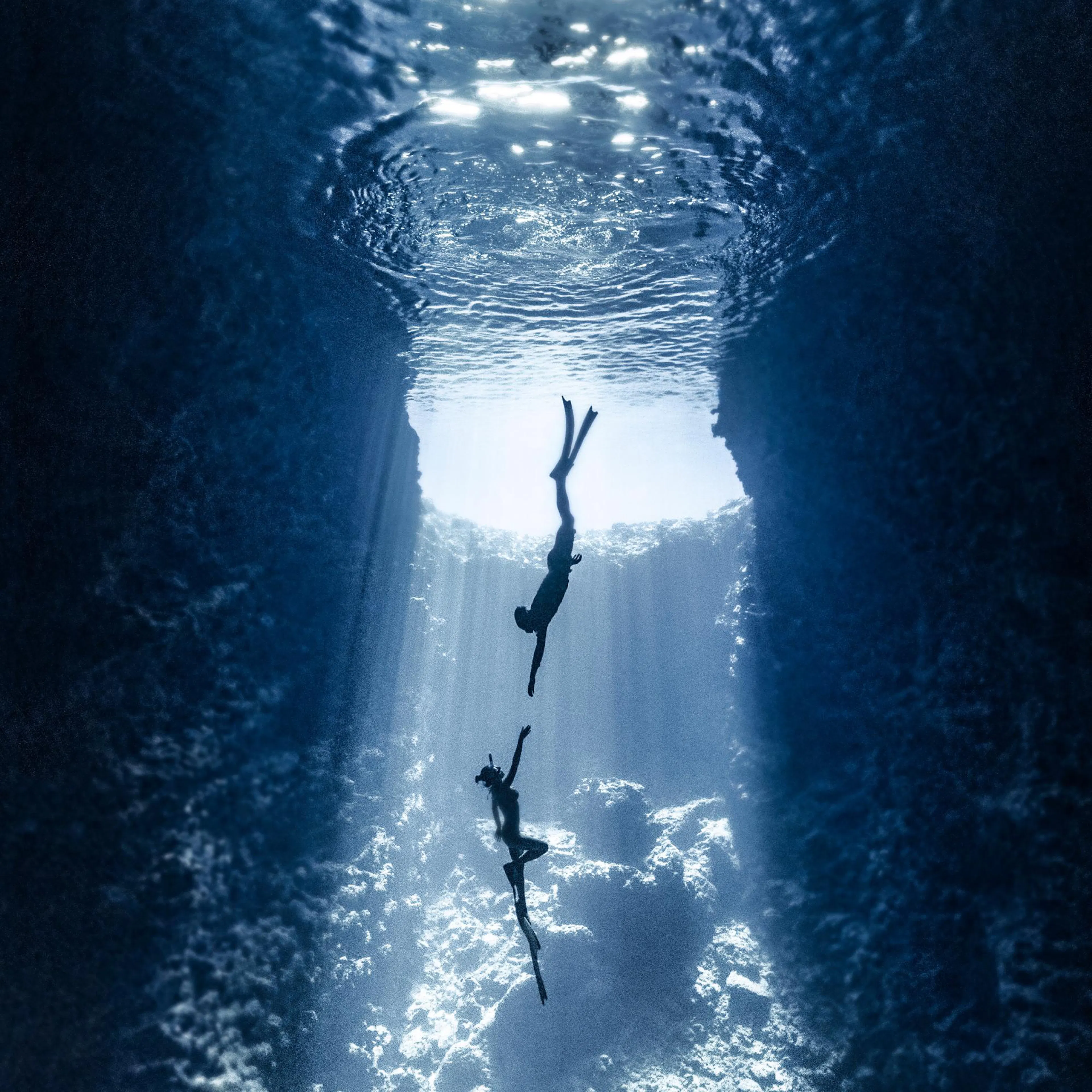 A poster depicting two free-divers reaching for each other in a dark blue underwater cave with light rays.