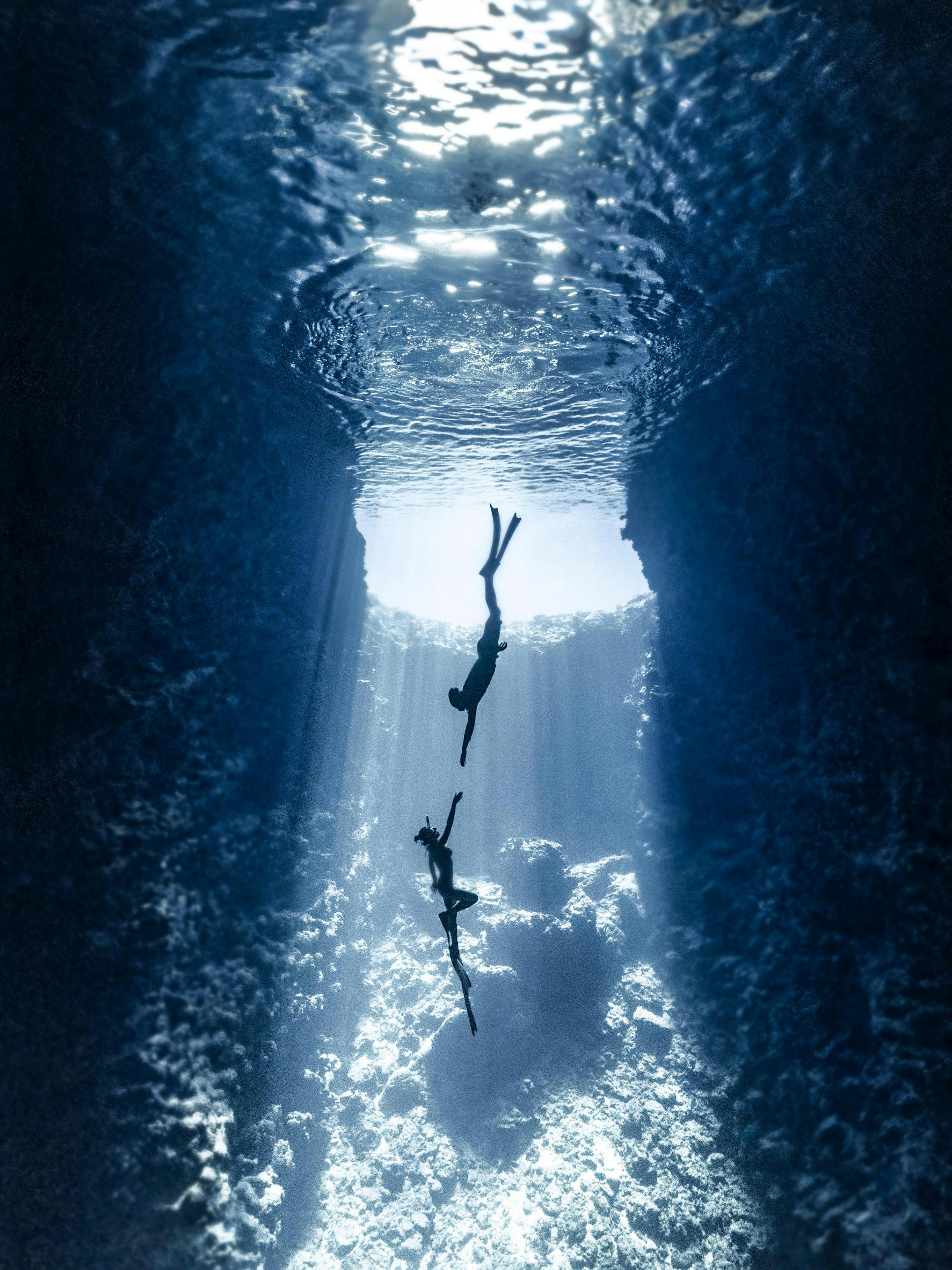 Póster de dos buceadores libres en un cenote submarino, con rayos de luz penetrando el agua azul.