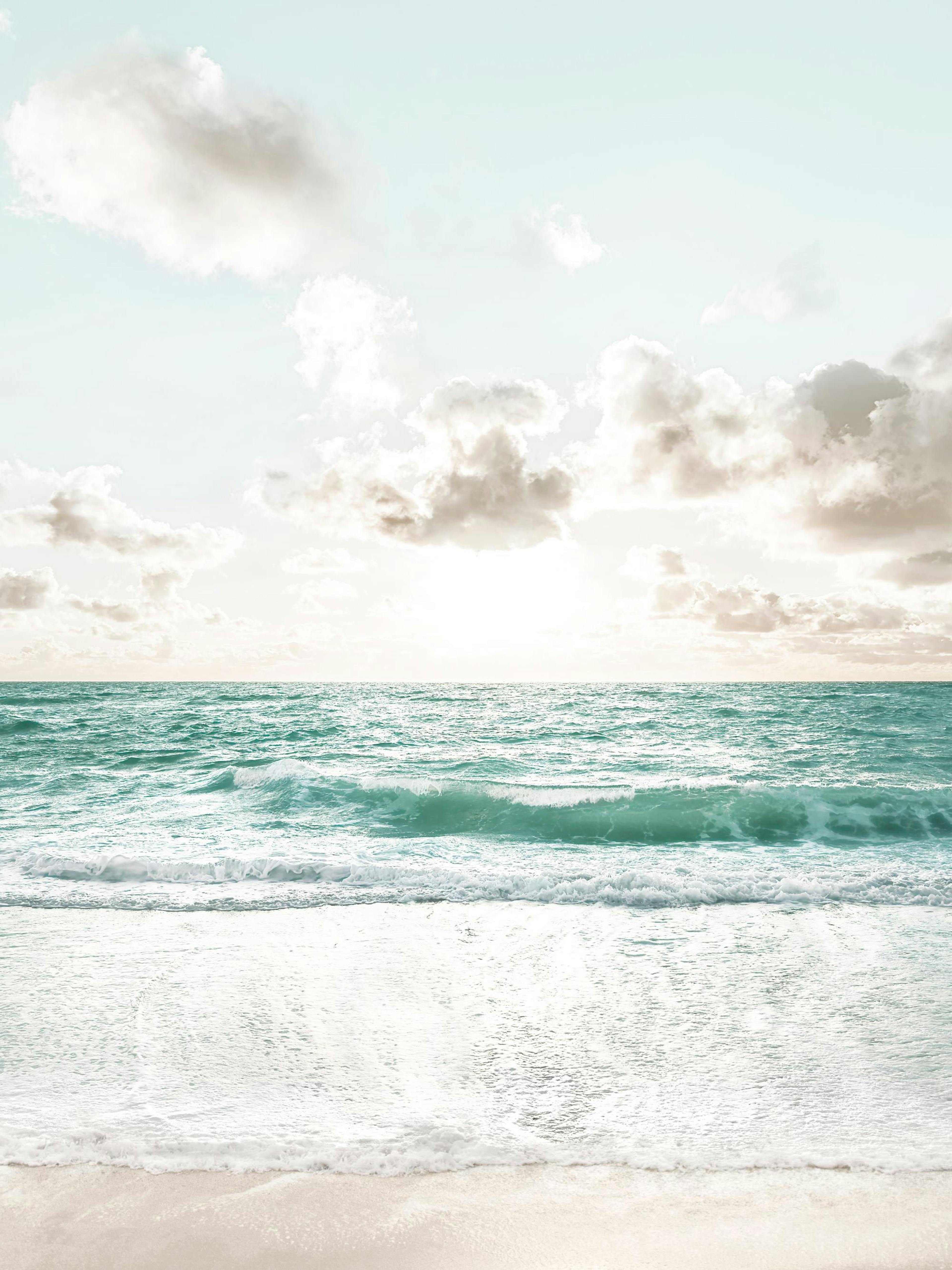 Póster de una playa con olas color turquesa, arena clara y un cielo azul pálido con nubes blancas.