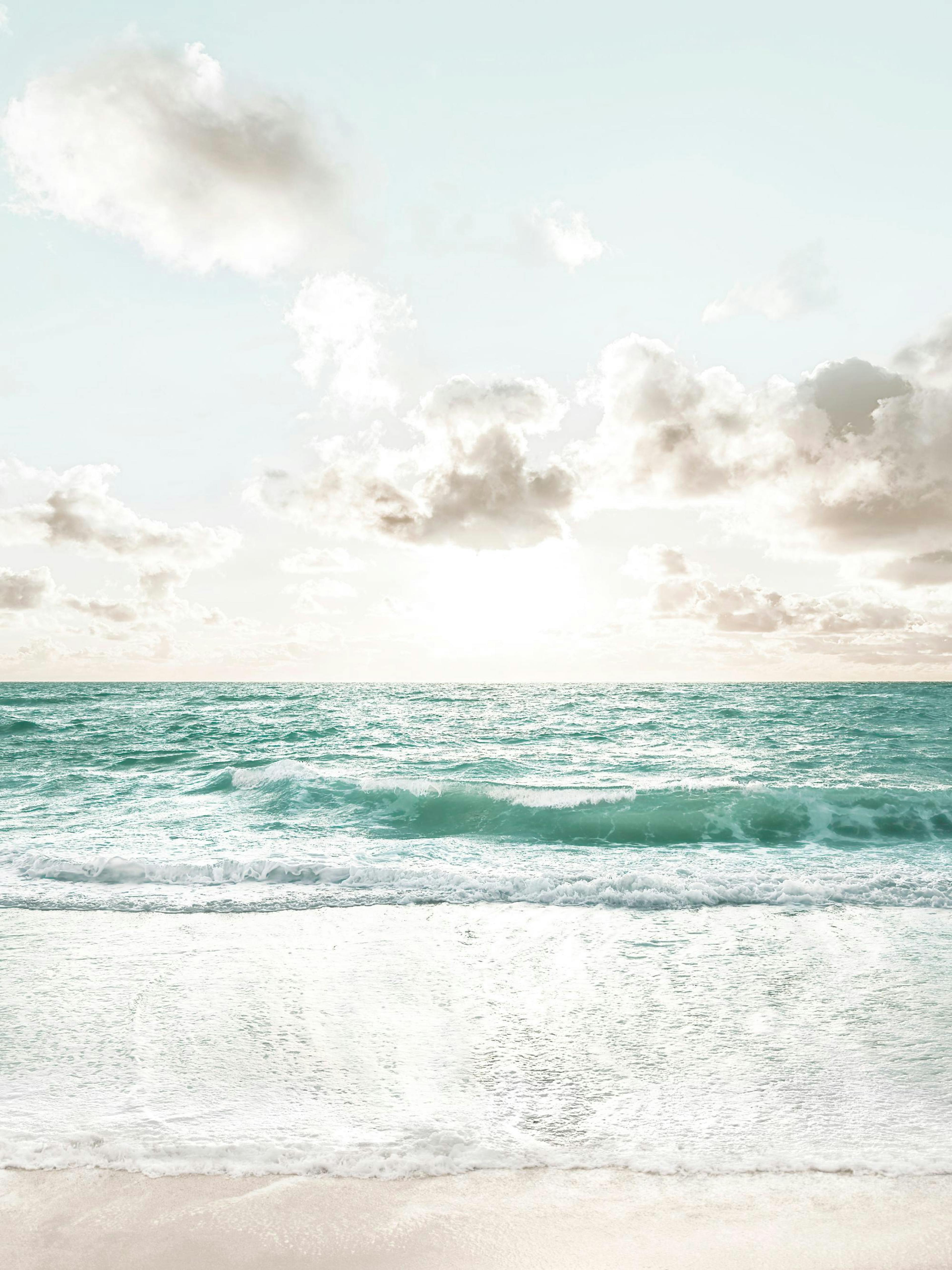 Poster dune plage avec vagues turquoise, sable clair et ciel nuageux au lever du soleil.