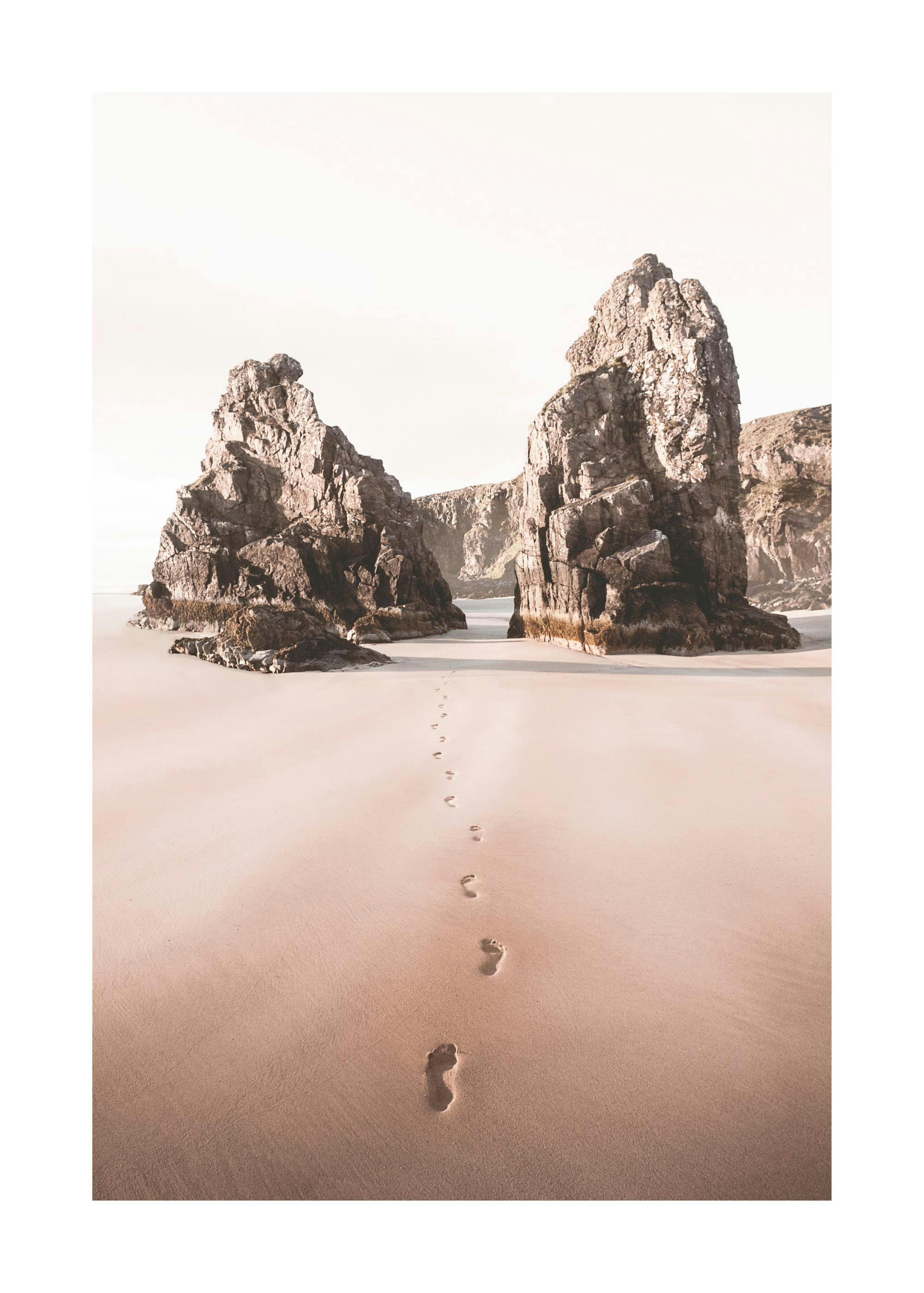 A poster featuring a beach with footprints leading to two large rock formations, under a bright sky.