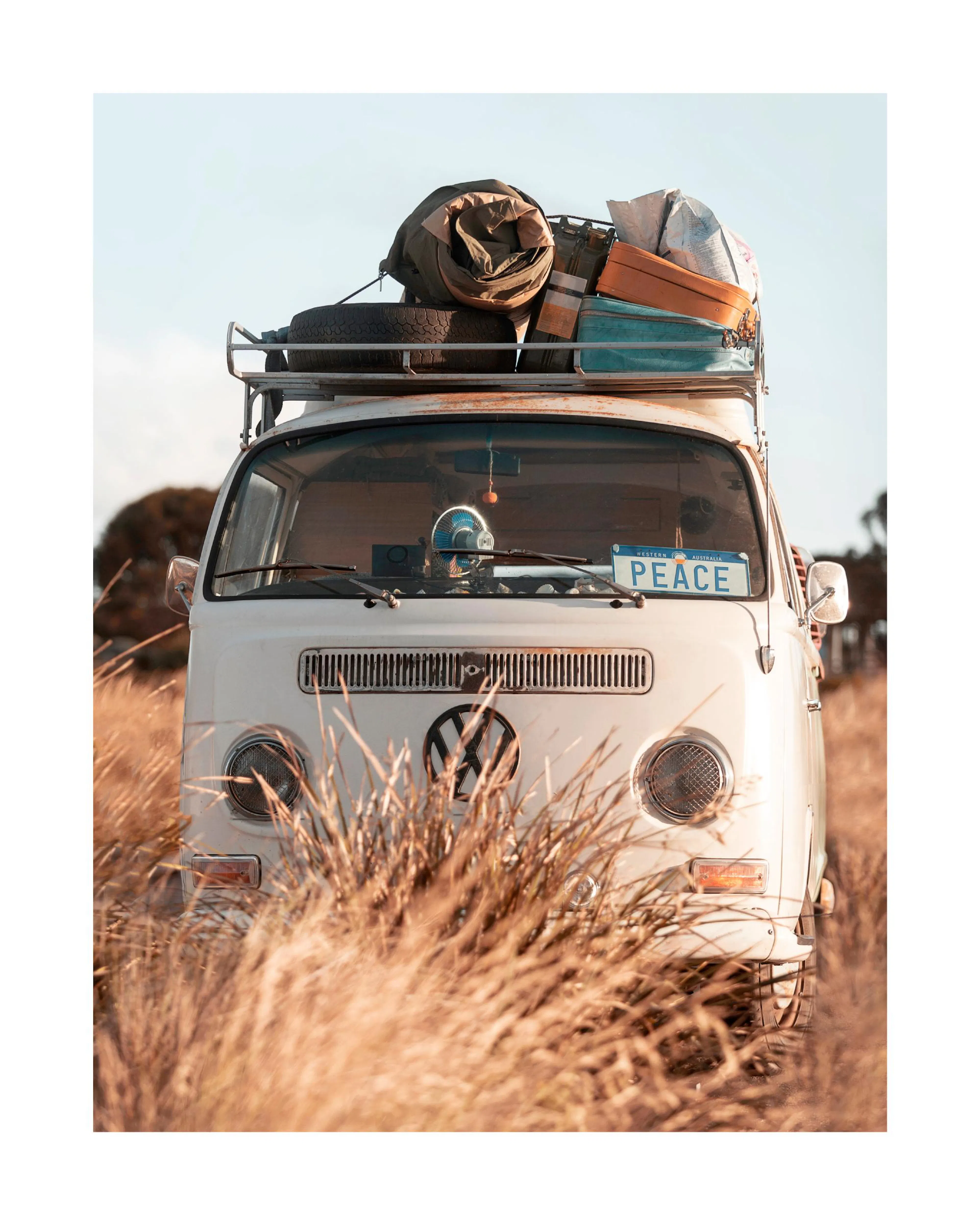 Poster dun van Combi VW blanc vintage chargé de bagages dans un champ de hautes herbes sèches, avec une plaque PEACE.