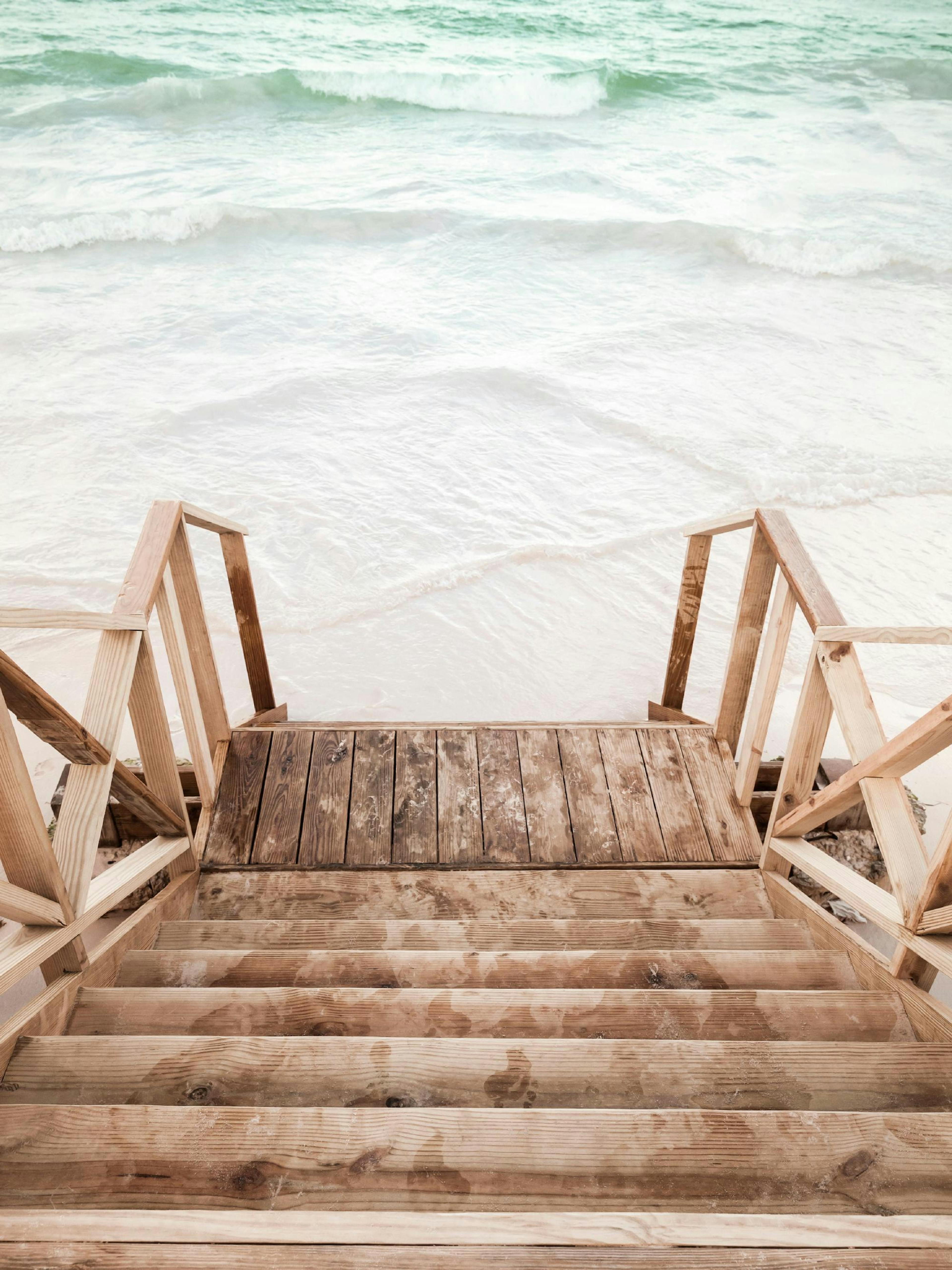A poster featuring wooden stairs and railings leading down to a white sandy beach with turquoise ocean waves.