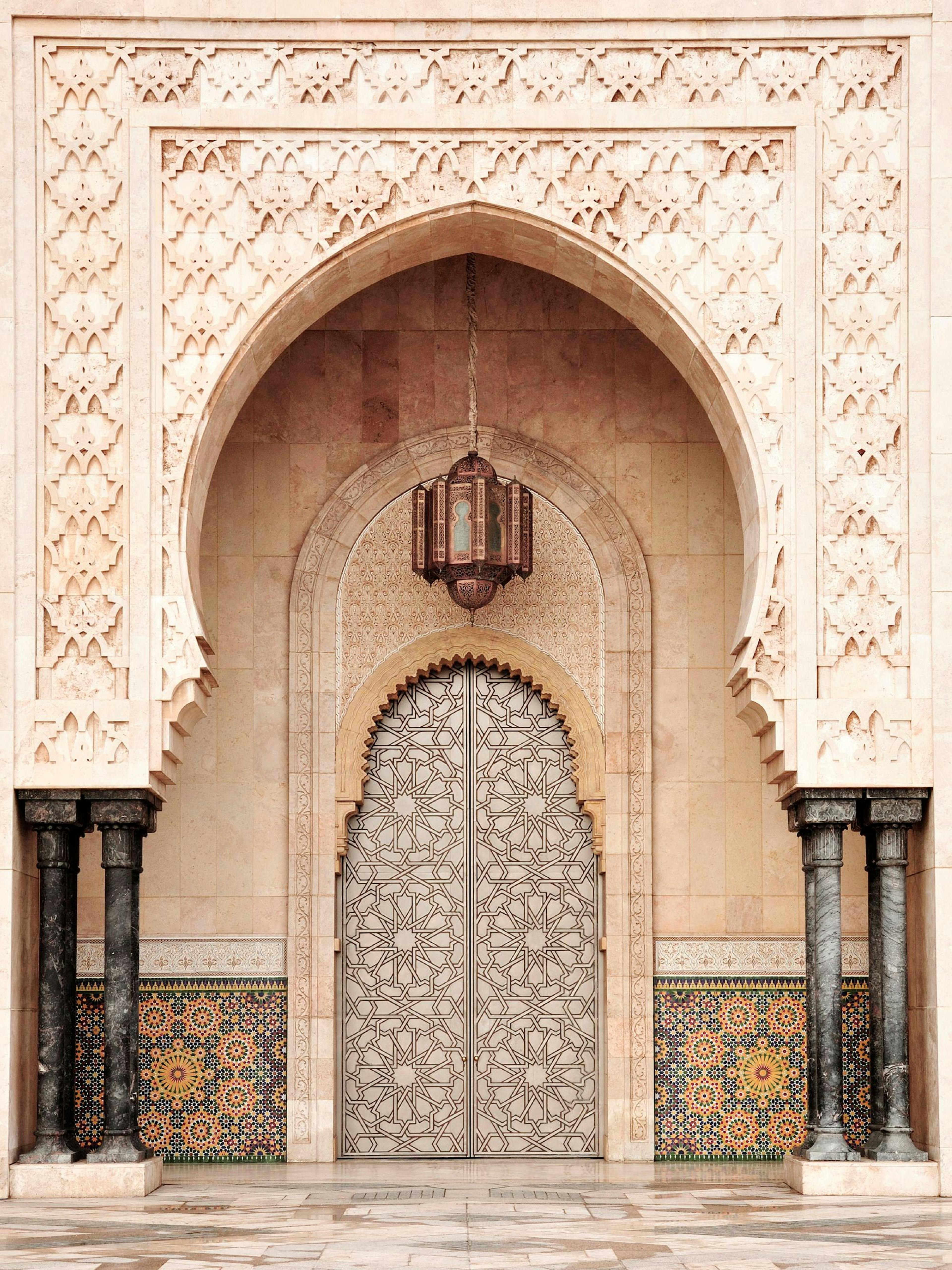 Plakat przedstawiający bogato zdobione marokańskie drzwi z łukiem i rzeźbionymi kolumnami.
