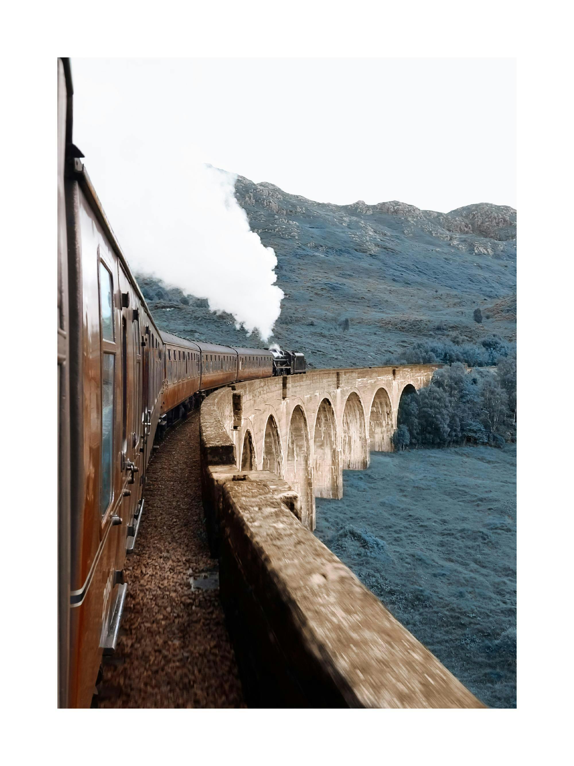 A poster featuring a steam train moving left to right over a stone arch viaduct, with misty blue mountains in the background.