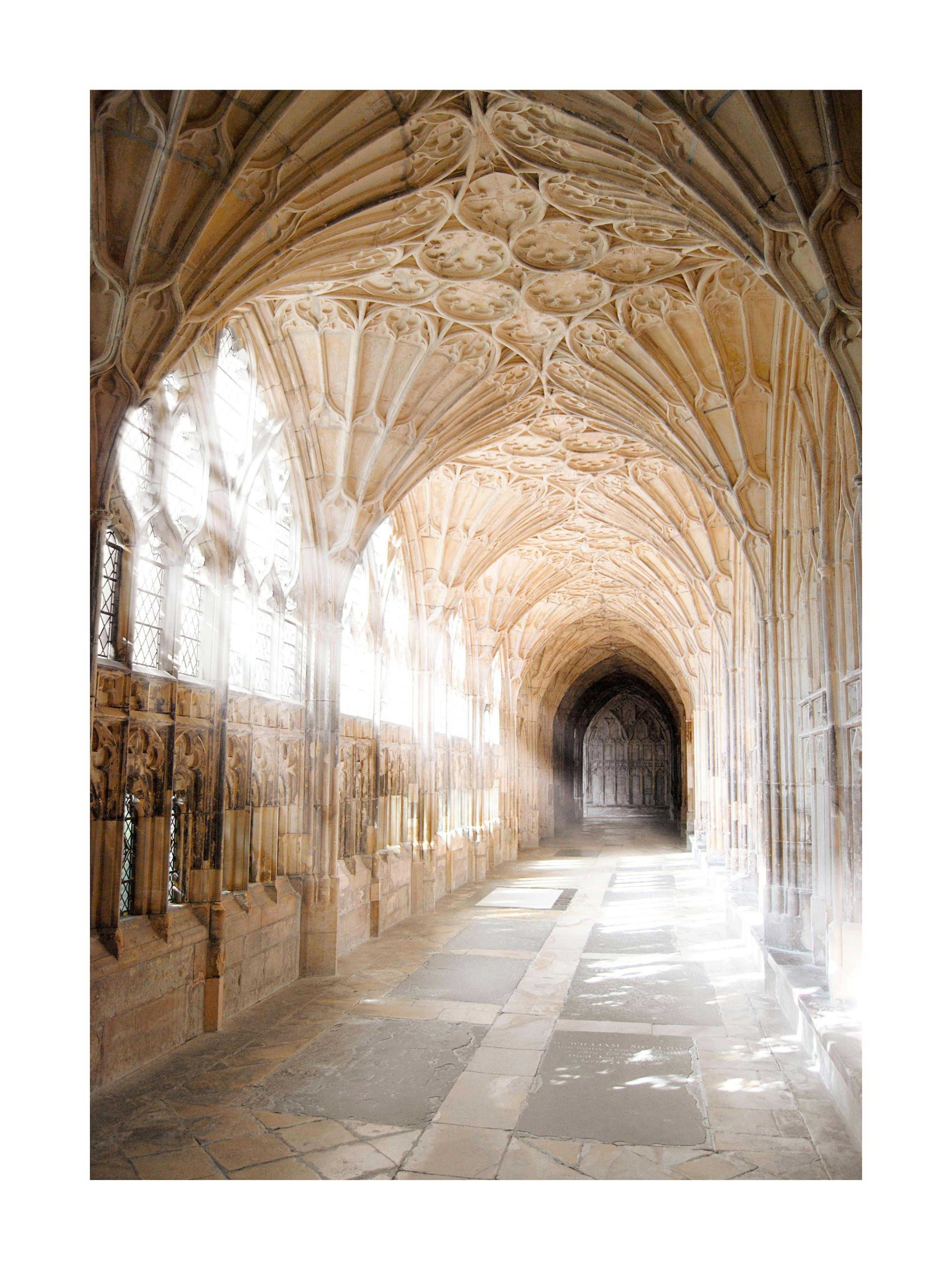 Póster de un pasillo gótico con arcos de piedra adornados y luz solar brillante que entra por las ventanas.