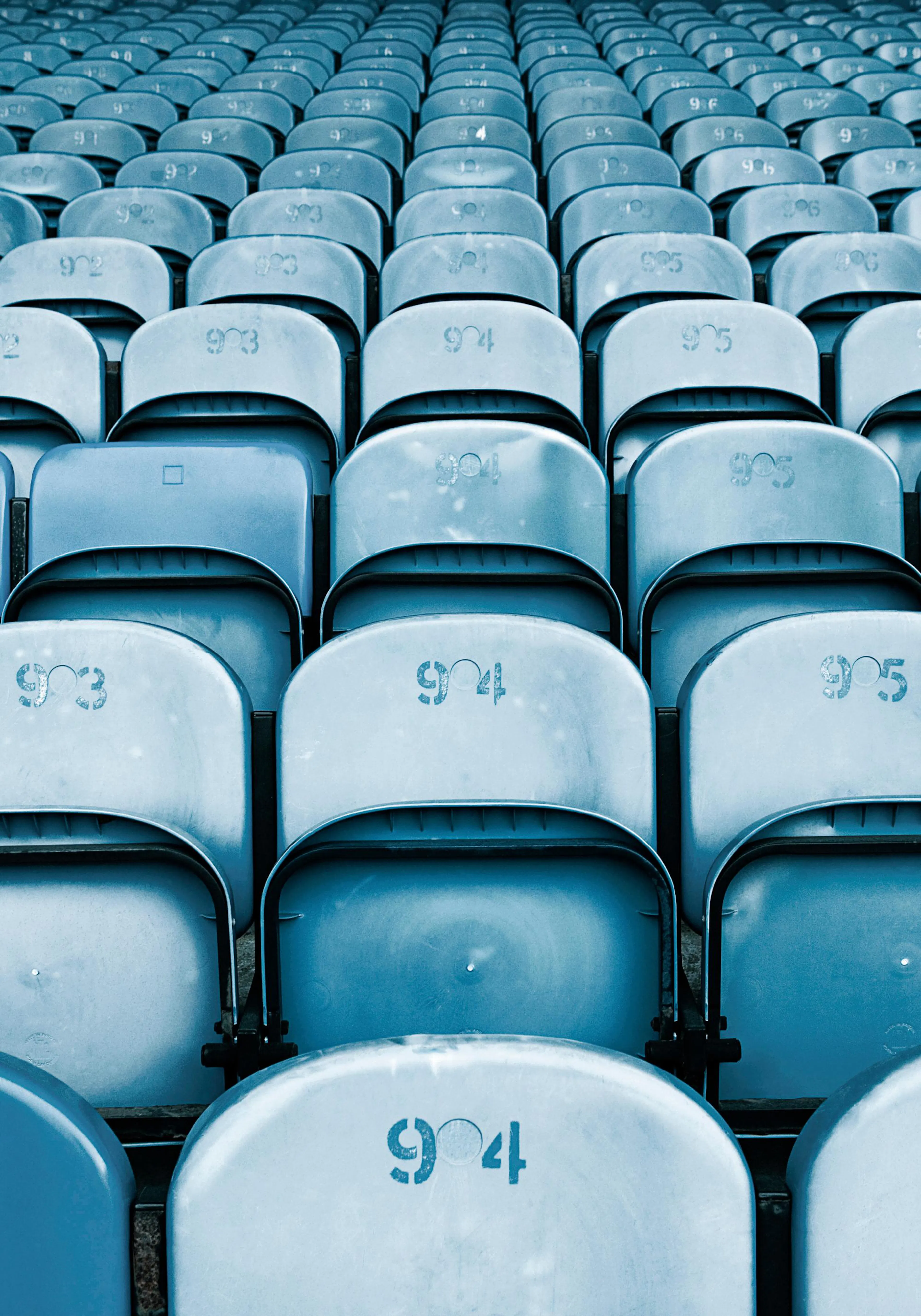 Kék stadionülések hosszú sorait ábrázoló poster, sorszámozott háttámlákkal.