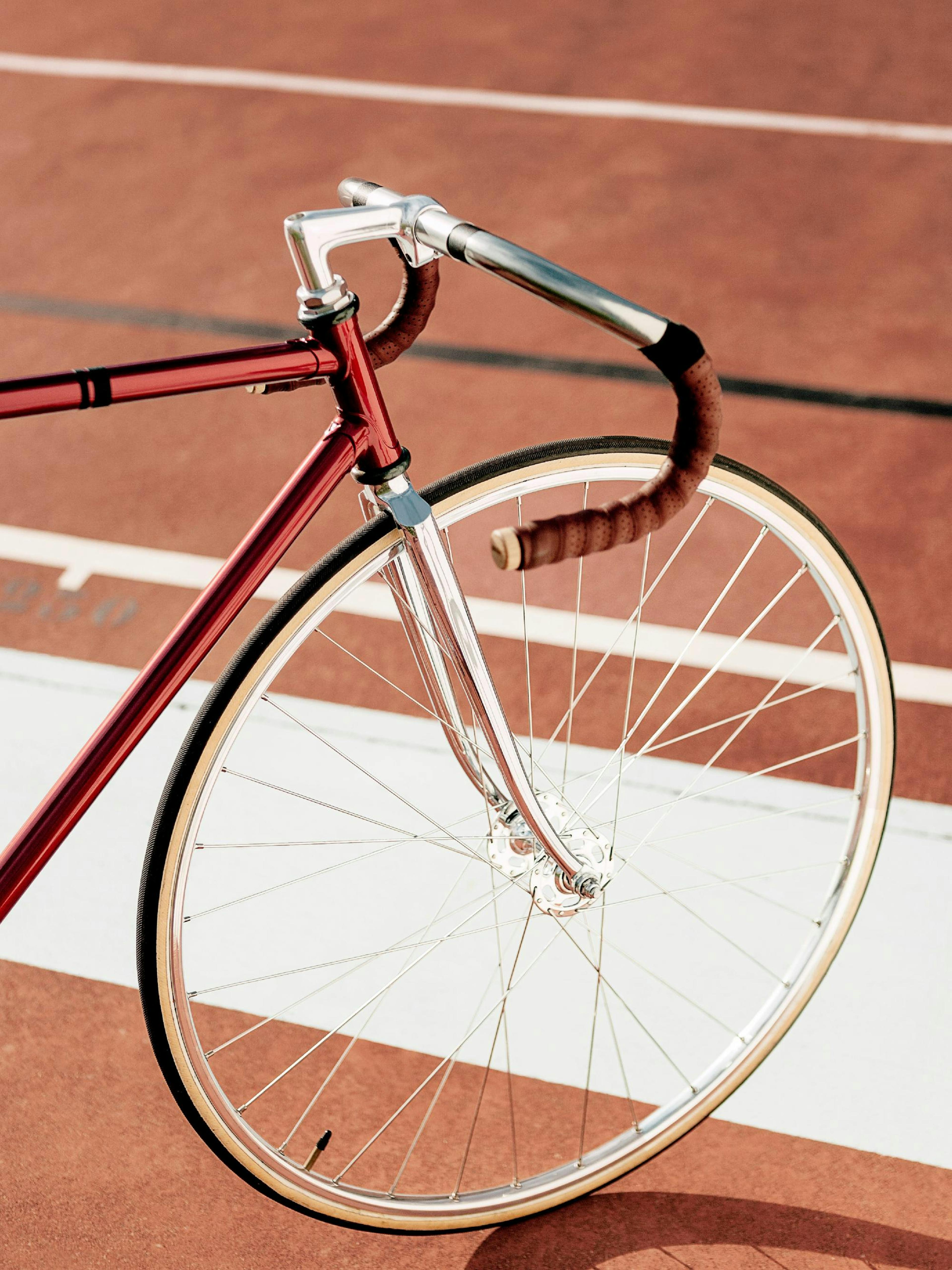 A poster featuring the front wheel and handlebars of a shiny red fixed-gear bicycle on a rust-red track.