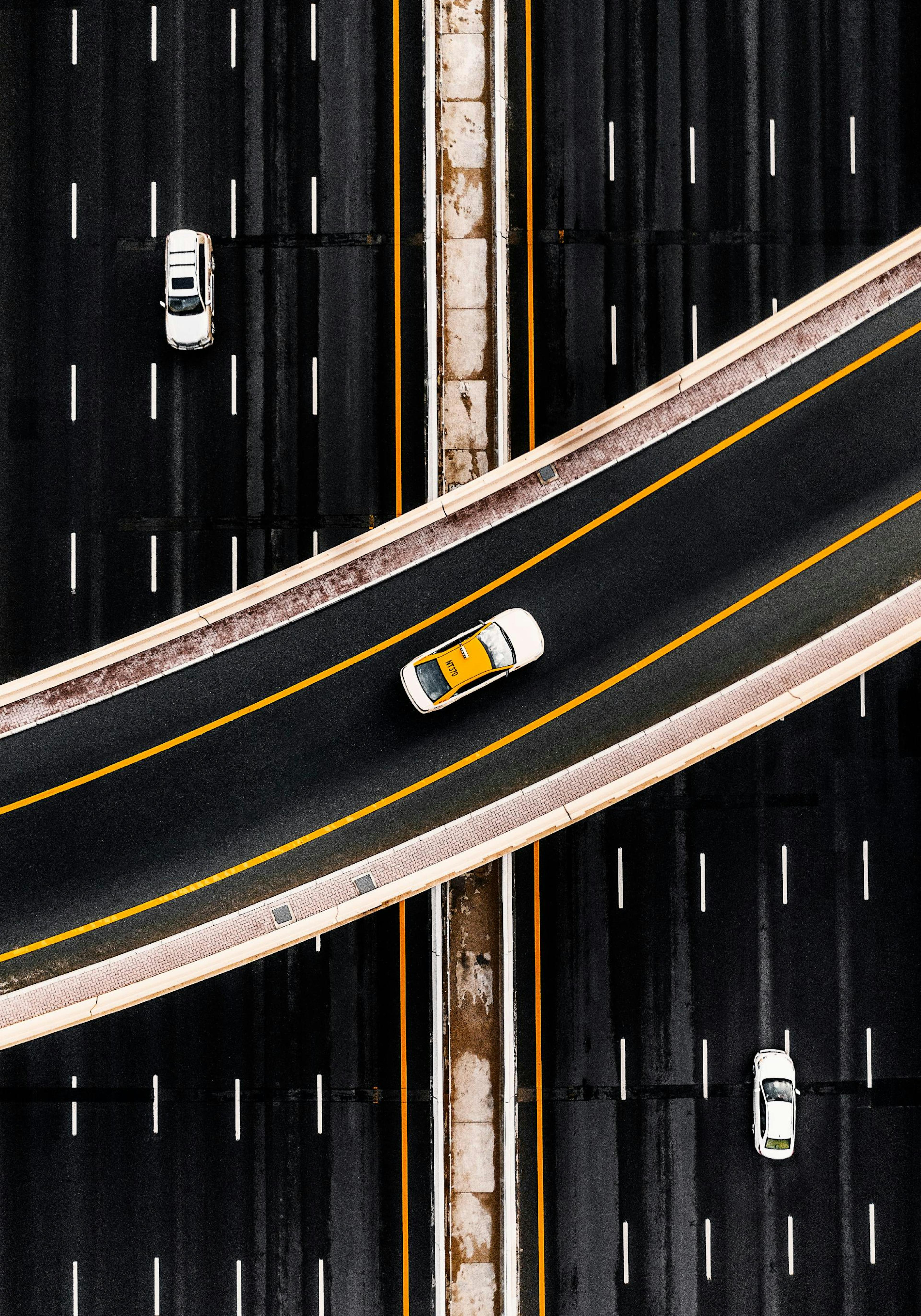 Póster de una vista aérea de una autopista con un taxi amarillo y dos vehículos blancos, líneas de carretera y barreras.