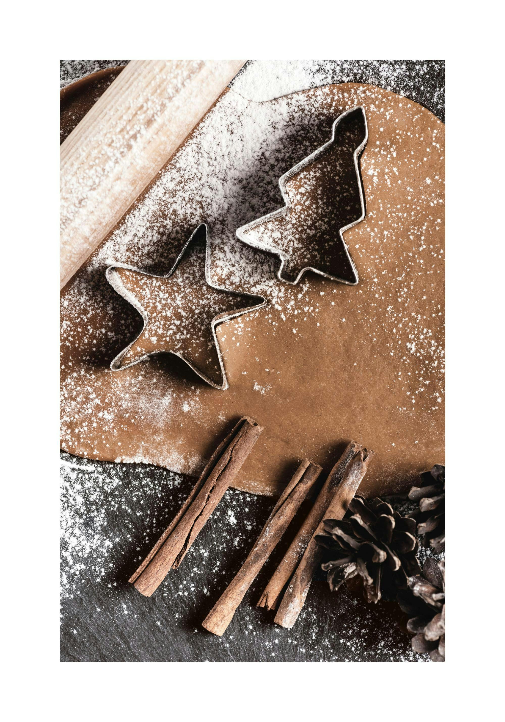 Ein Poster mit Lebkuchenteig, Ausstechformen, Zimtstangen und Tannenzapfen, bestreut mit Puderzucker.