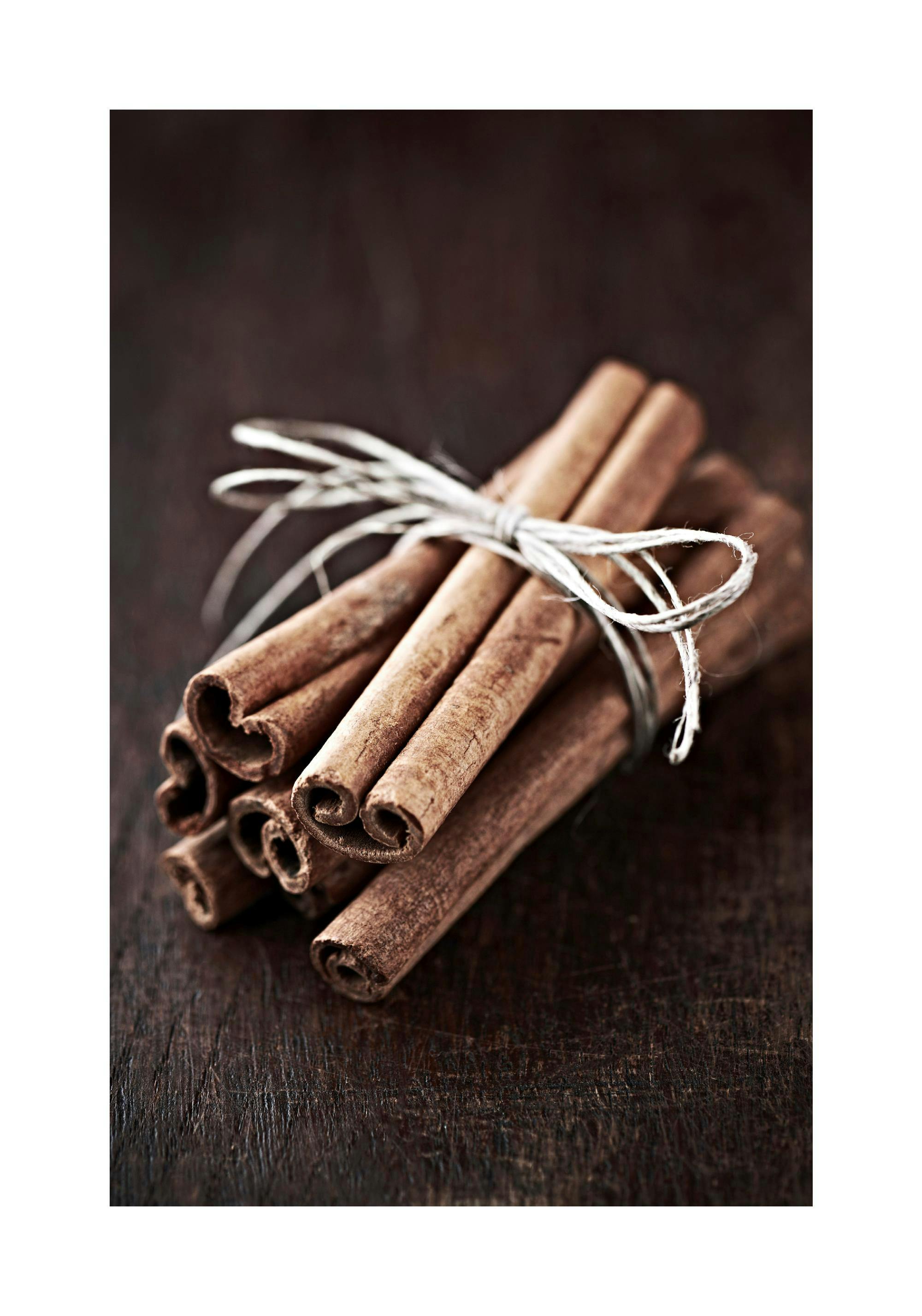 Poster mit zimtbraunen Zimtstangen, die mit einer Schnur gebunden auf einem dunklen Holztisch liegen.
