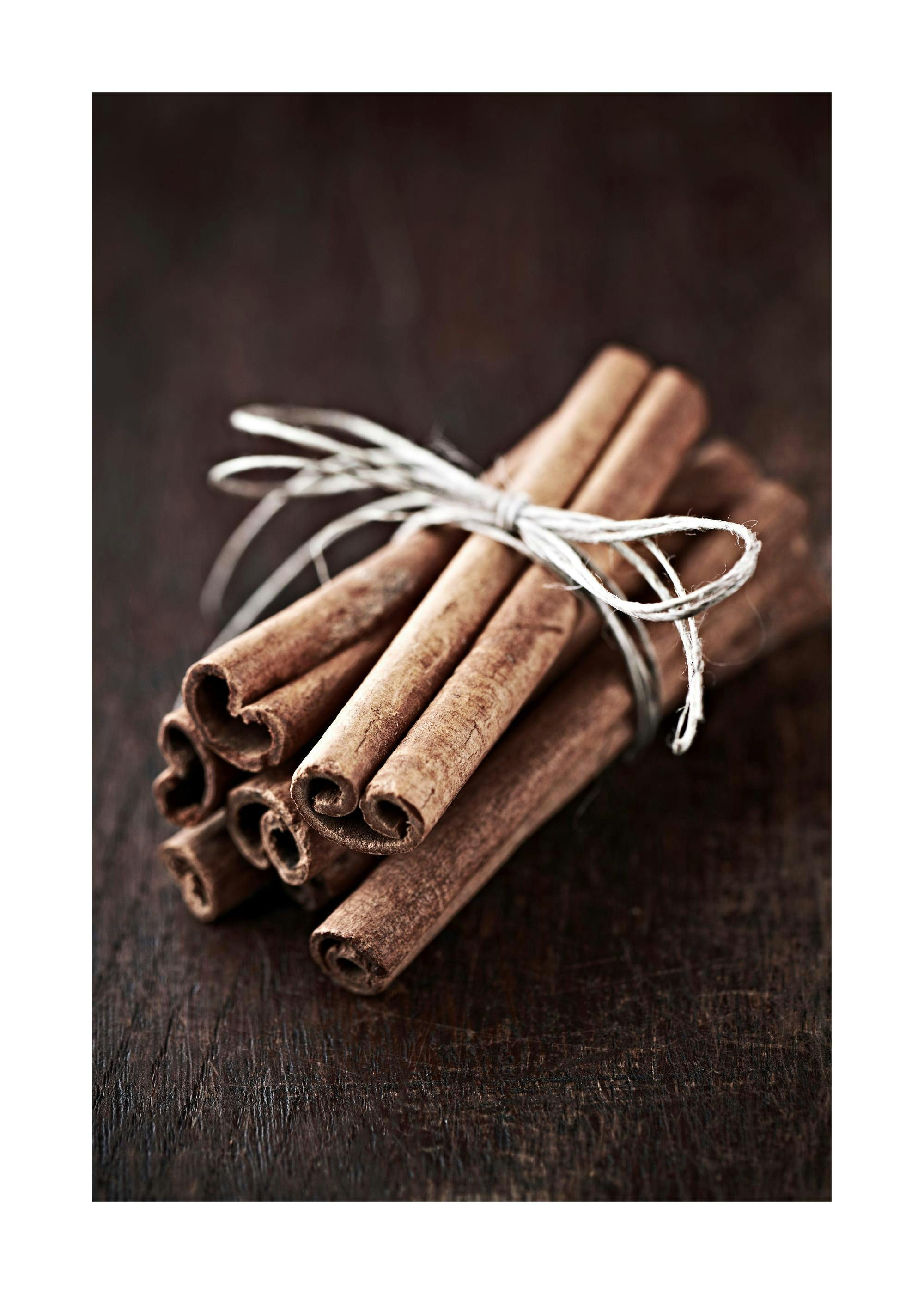 A poster featuring a bundle of cinnamon sticks tied with white string on a dark wooden surface.