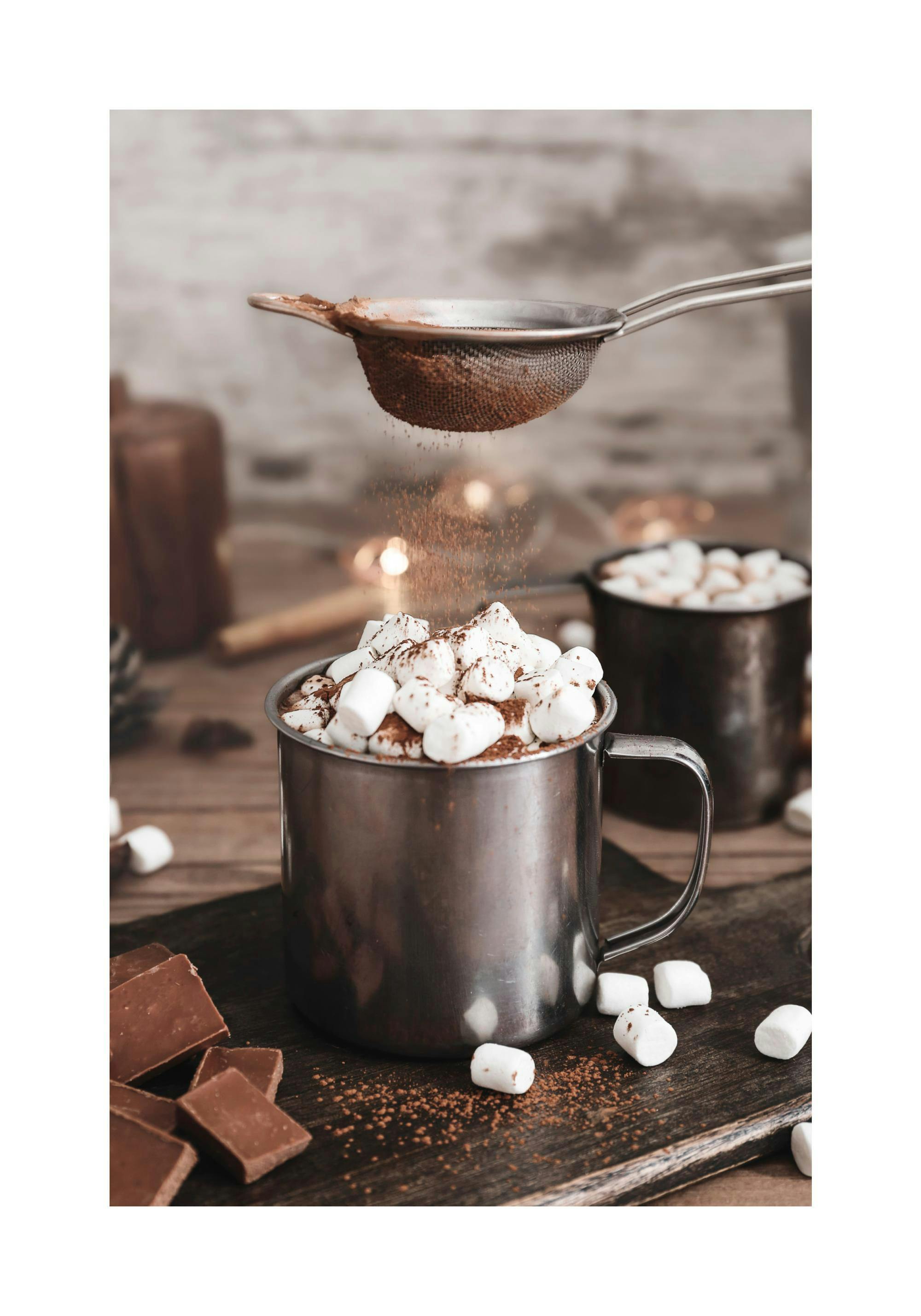 Ein Poster mit einer Tasse heißer Schokolade, verziert mit Marshmallows und Kakaopulver, auf einem Holztisch.