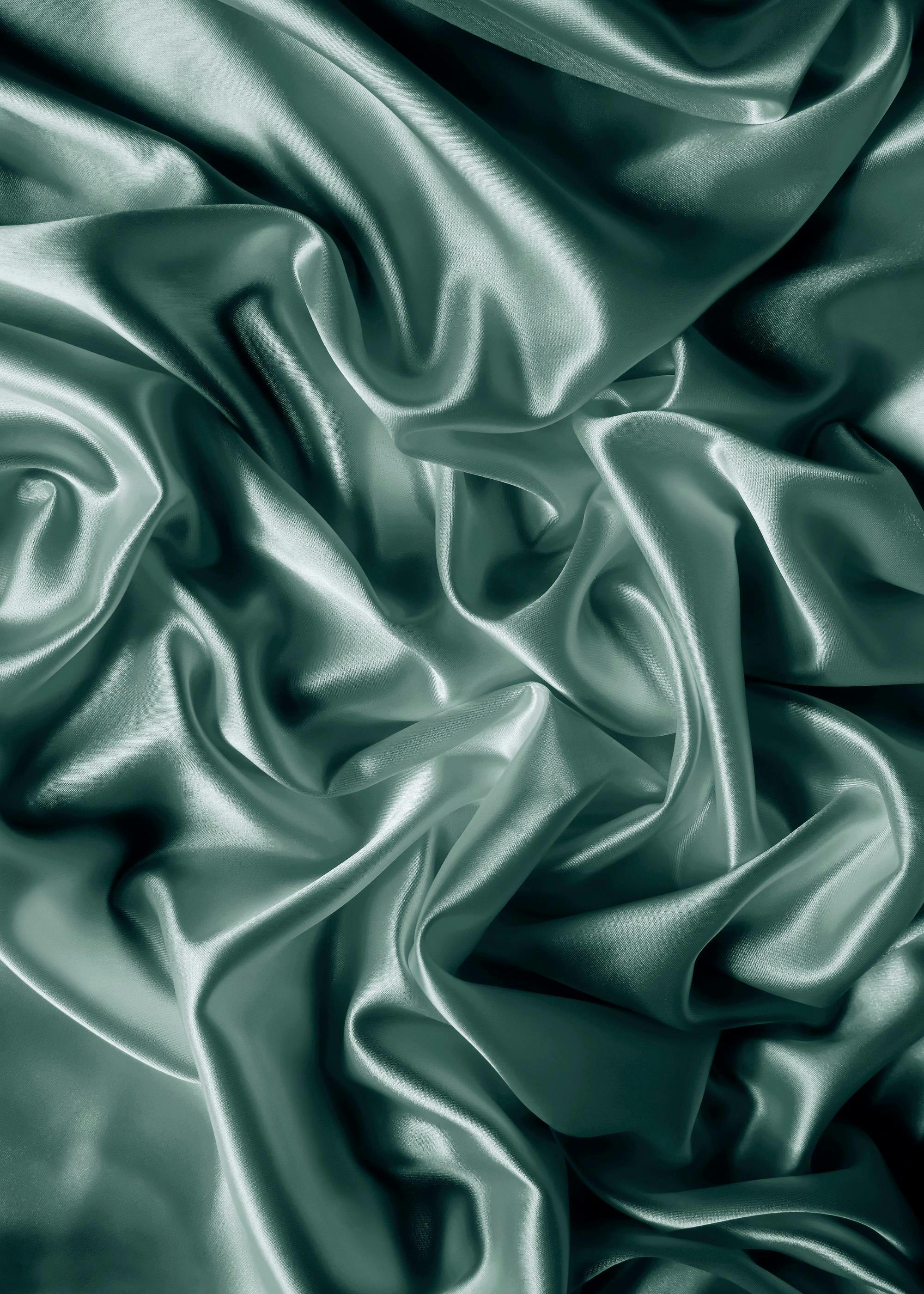 A poster featuring a luxurious draped satin fabric in a deep teal green color, showcasing the folds and sheen.