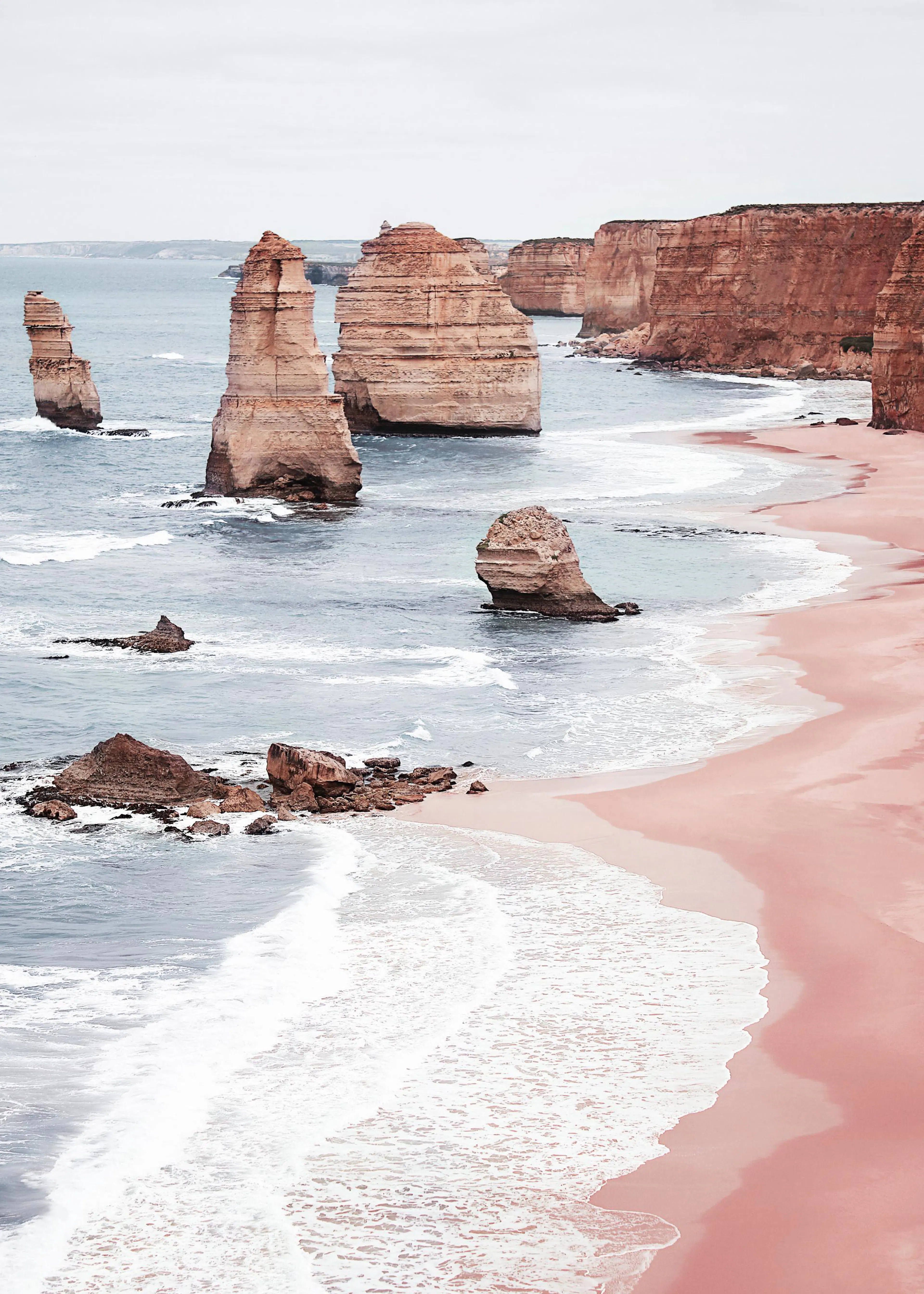 A poster az Ausztráliai Tizenkét Apostol szikláiról, ahol a tengerparti sziklák és a homokos rózsaszín part találkozik a tengerr