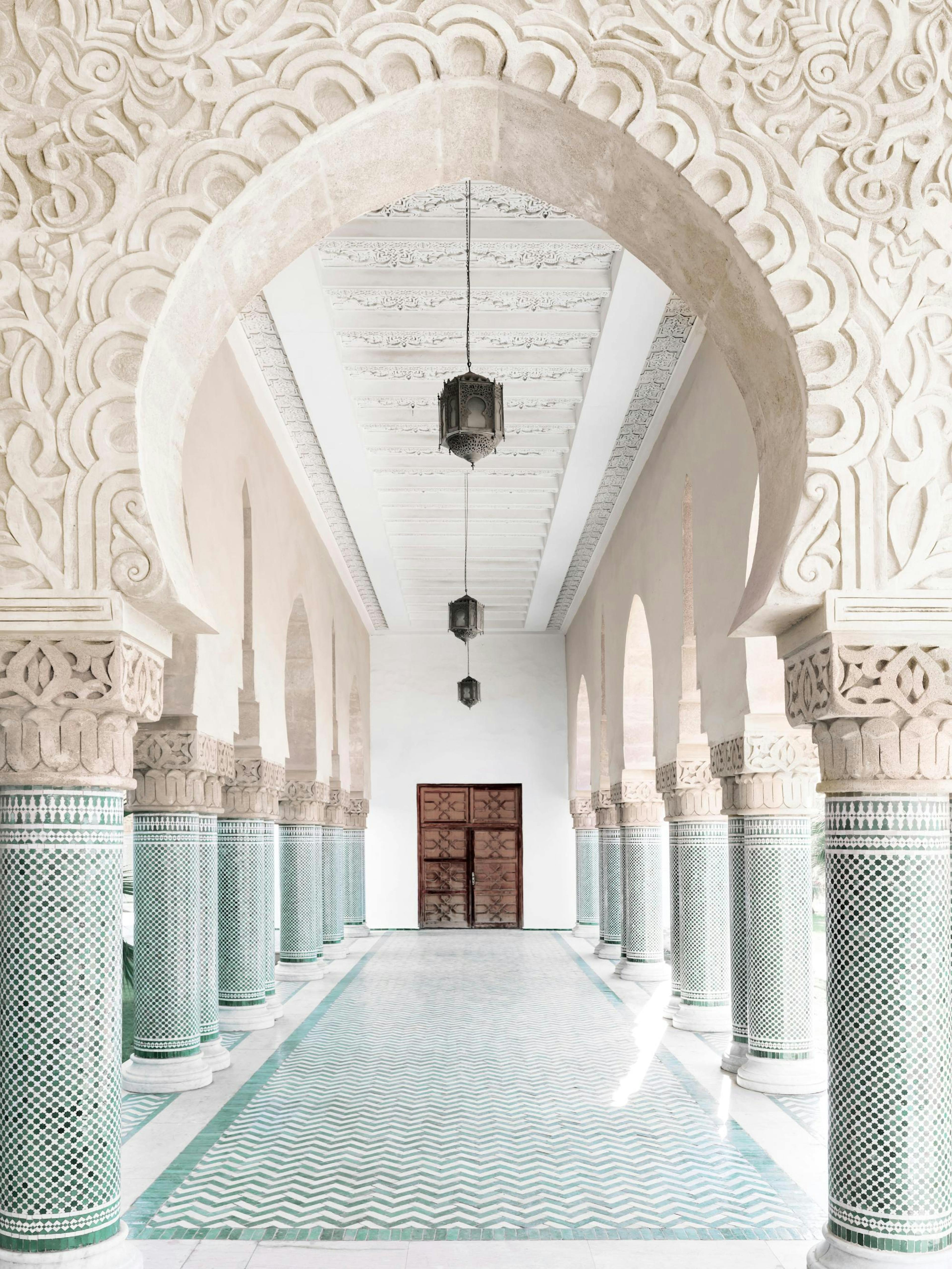 Un póster de un corredor marroquí con arcos ornamentados, columnas de azulejos verdes y puertas de madera.