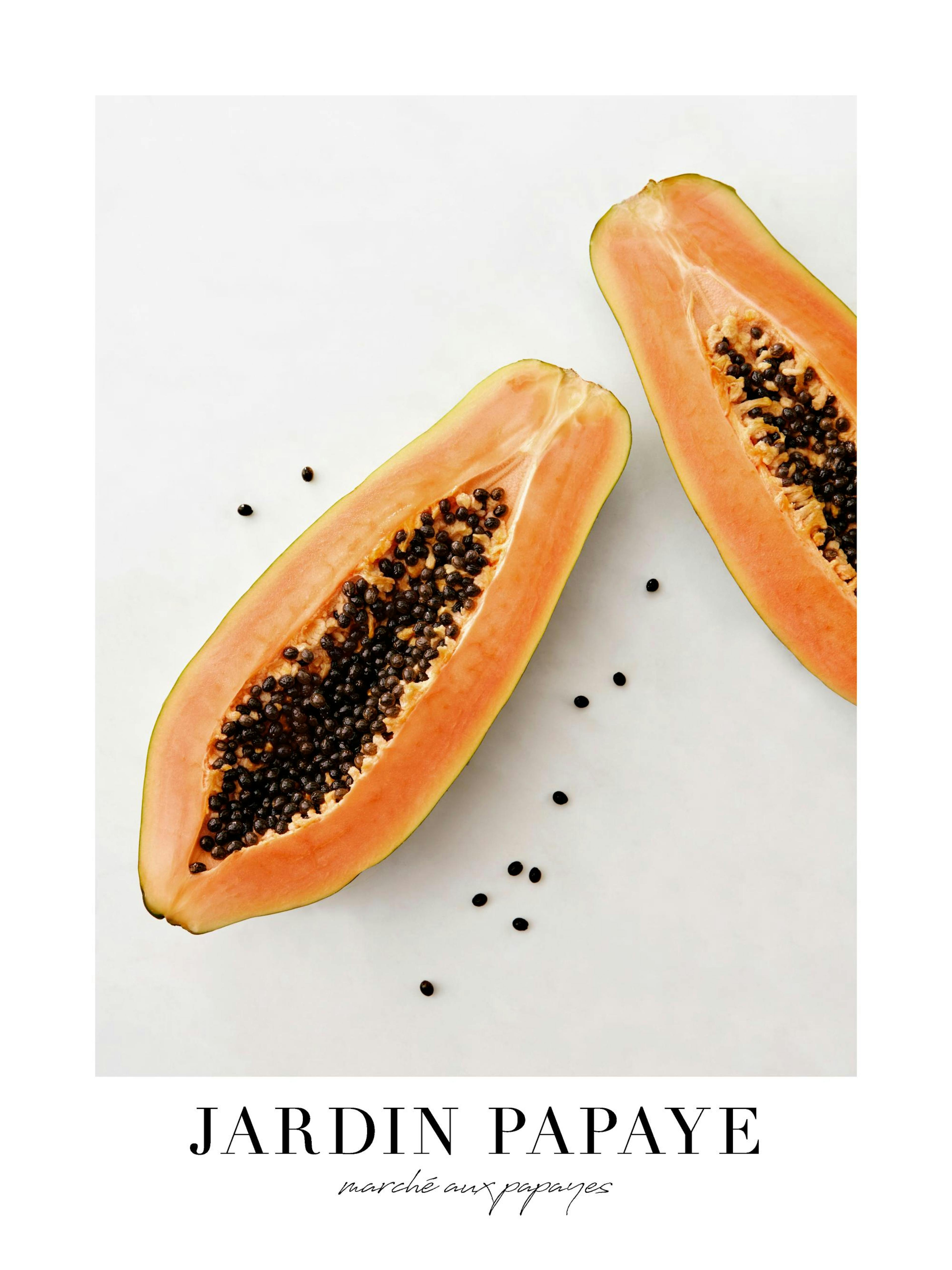 A poster featuring two halves of a papaya with seeds on a light background, hanging above a round table with a book and mug.