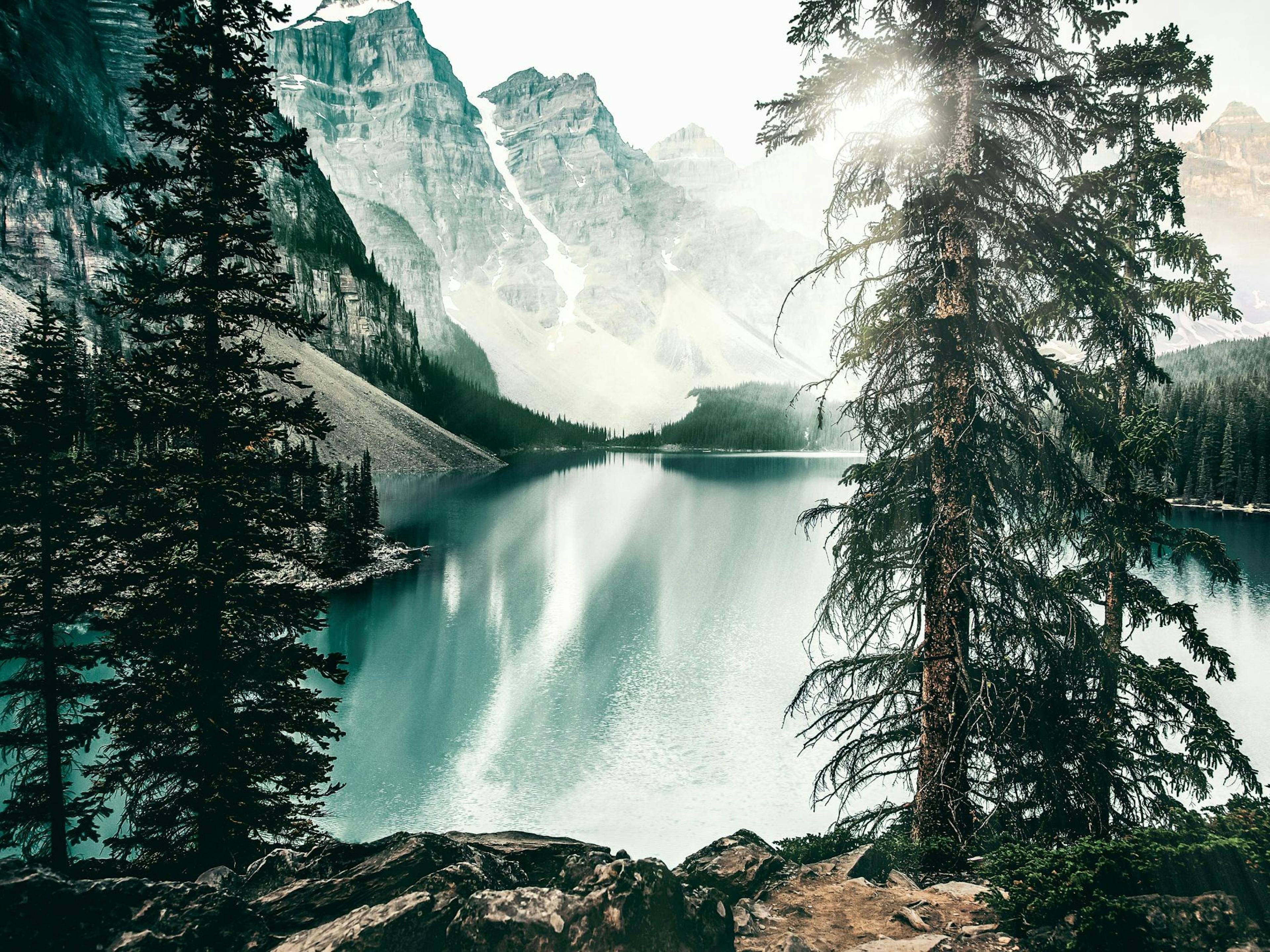 A stunning poster of Moraine Lake with turquoise water, surrounded by evergreen trees and snow-capped mountains under a bright s