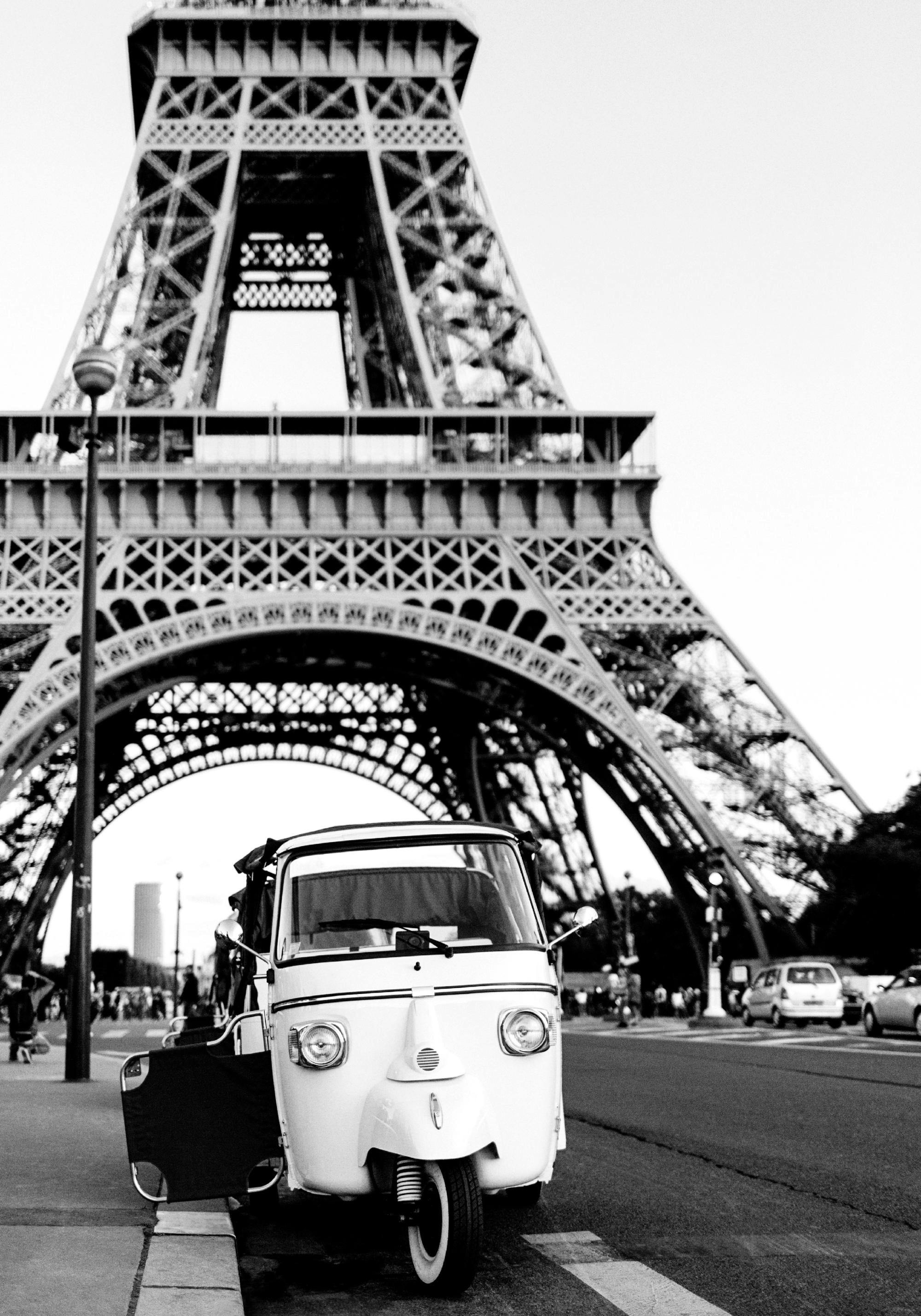 En plakat i svart-hvitt av Eiffeltårnet og en hvit trehjulet moped i forgrunnen.