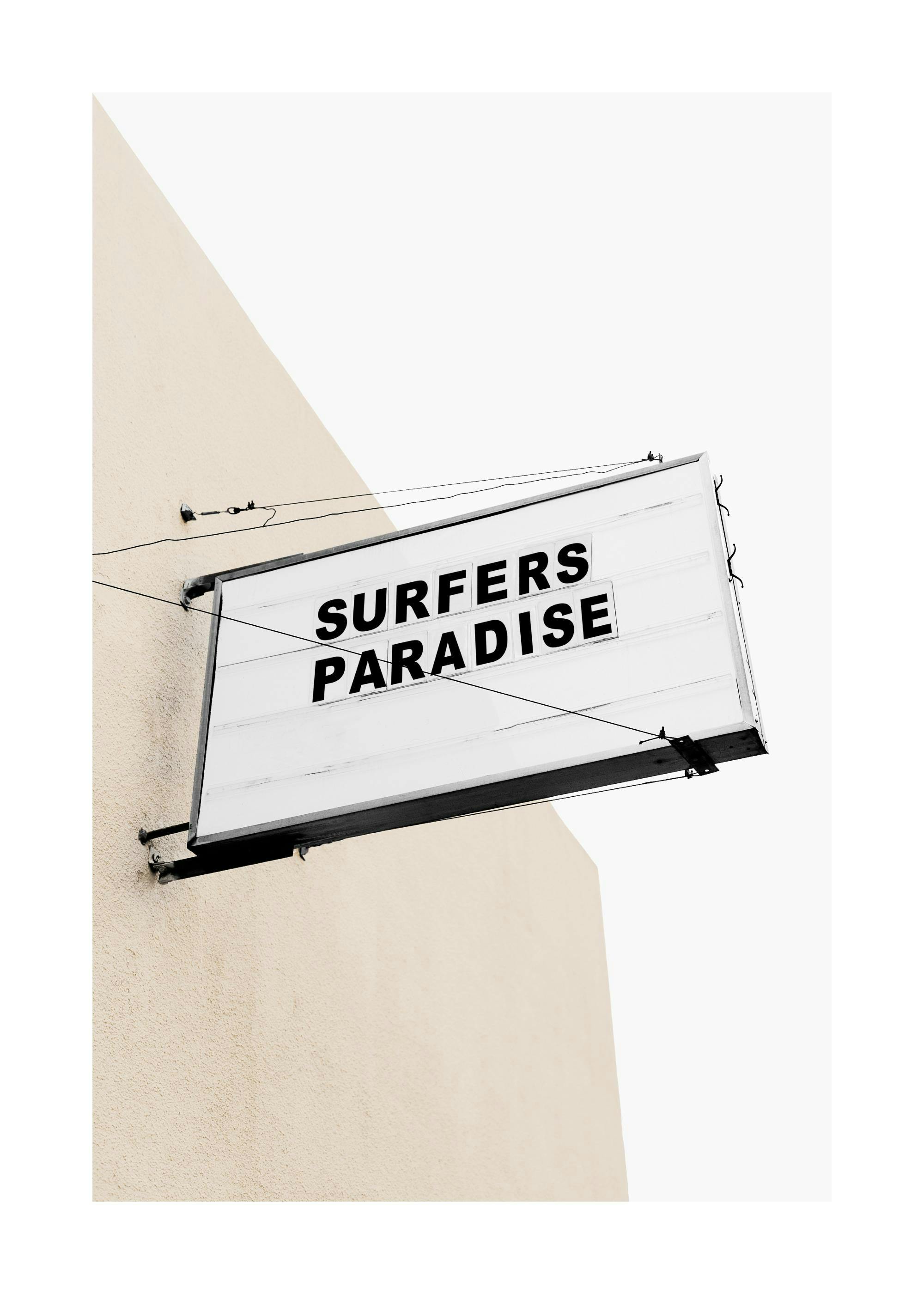 Ein Poster mit einer beleuchteten Werbetafel mit der Aufschrift SURFERS PARADISE auf einer beigen Wand.