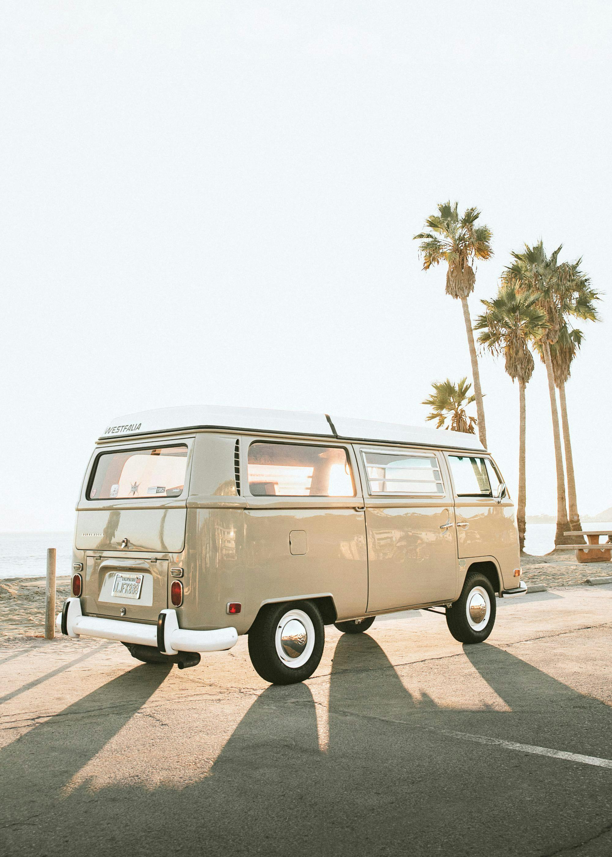 Poster eines beigefarbenen VW Busses am Strand mit Palmen im Sonnenuntergang.
